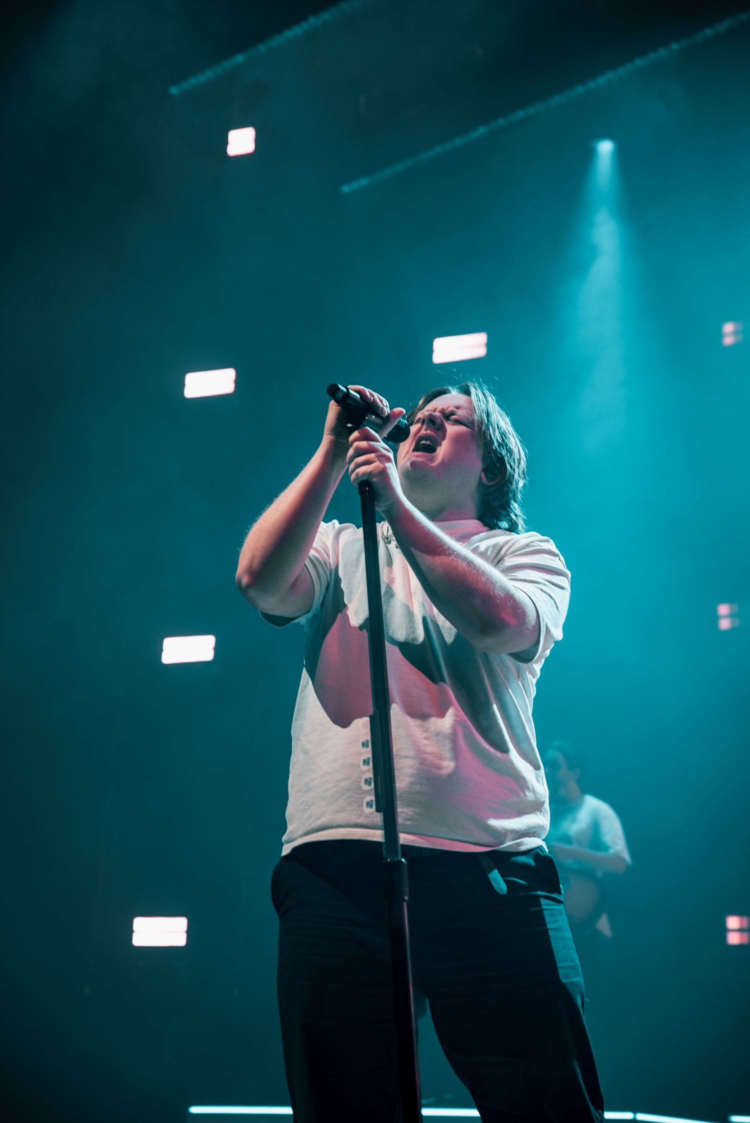 Concert stage bathed in teal lighting as performer delivers emotional vocal performance.