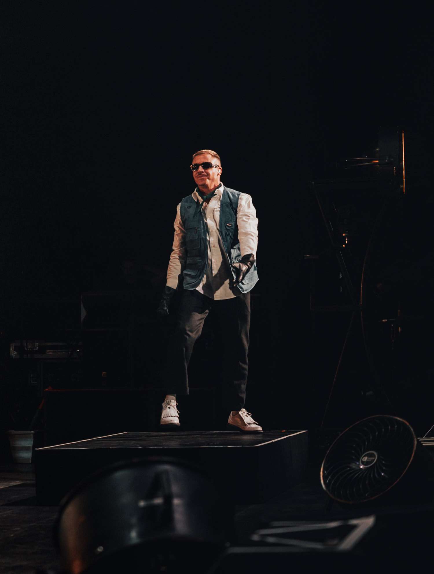 Stage performer in white vest and dark pants crouches during dramatic performance.