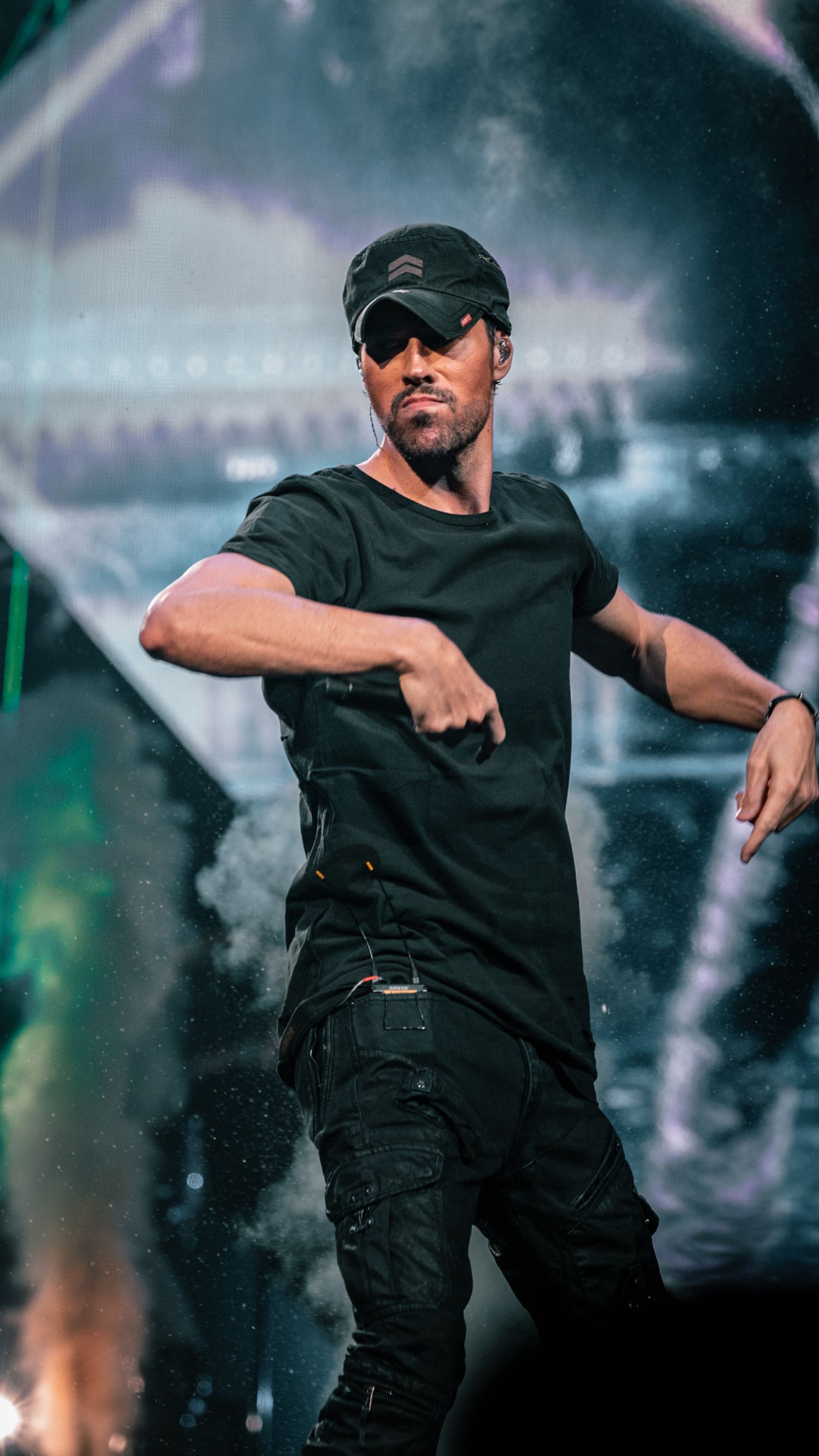 Performer in black outfit dancing on stage with atmospheric lighting and smoke effects.