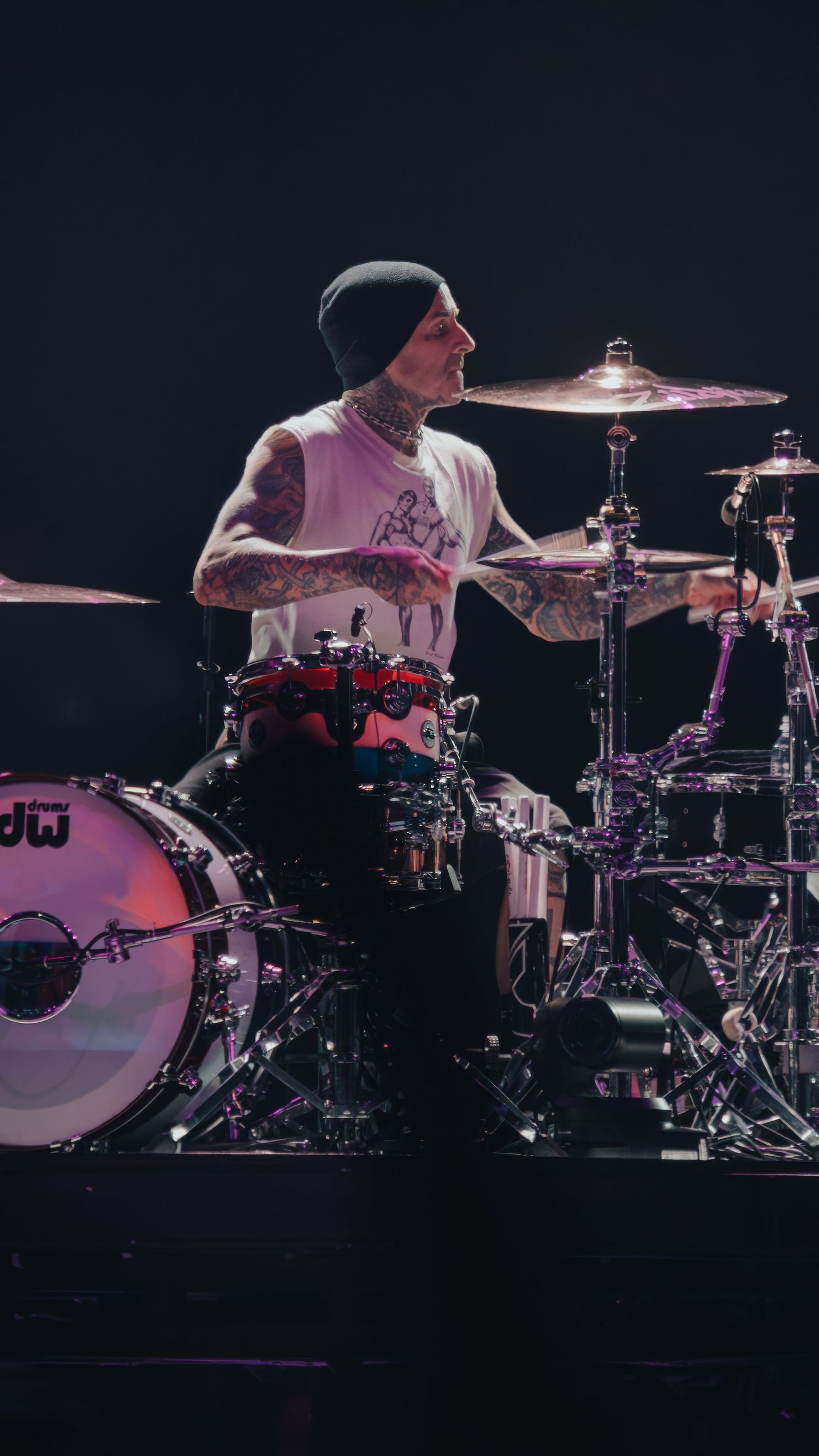 Drummer plays energetically on illuminated stage with purple lighting effects.