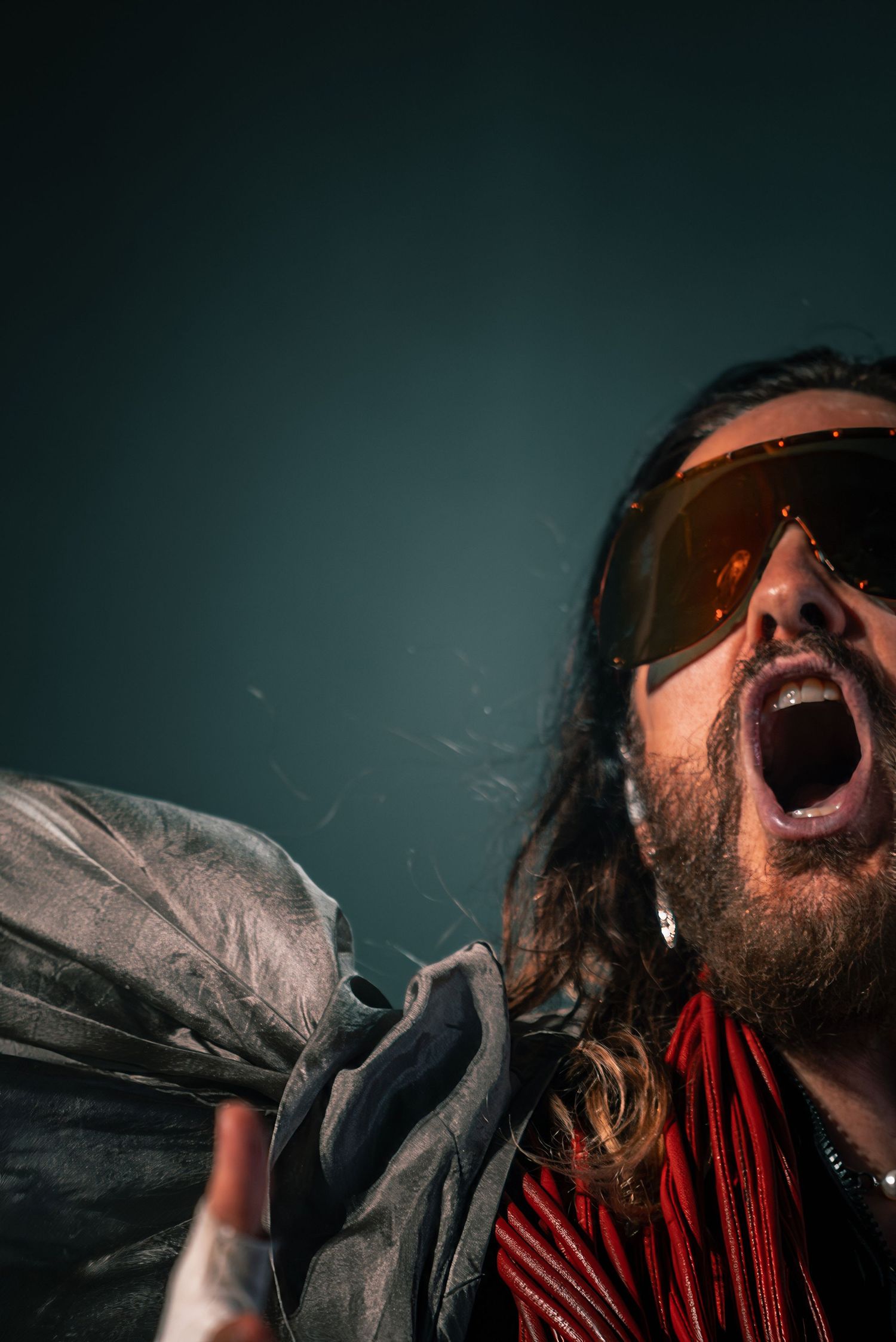 Close-up of a performer wearing sunglasses and red accessories shouting into microphone.