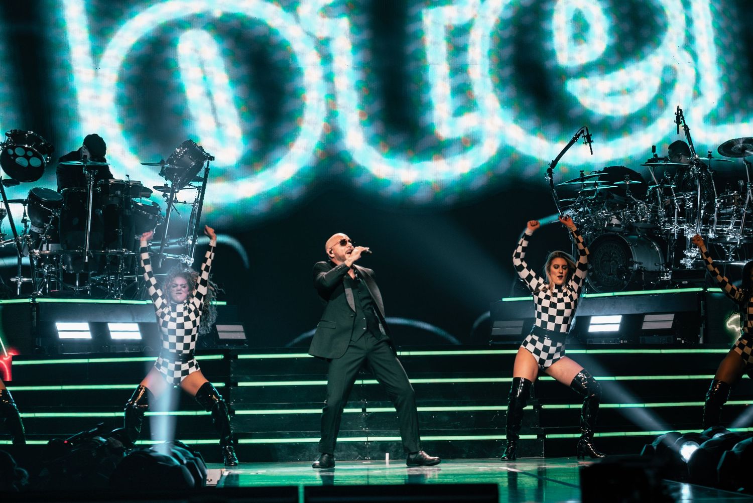 Concert stage with blue neon lighting and checkered pattern performers.