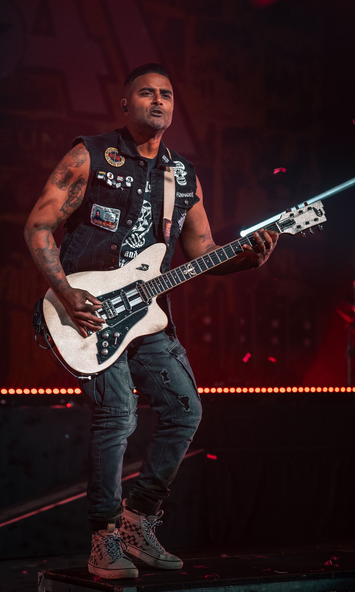 Guitarist plays white electric guitar while performing on illuminated concert stage.