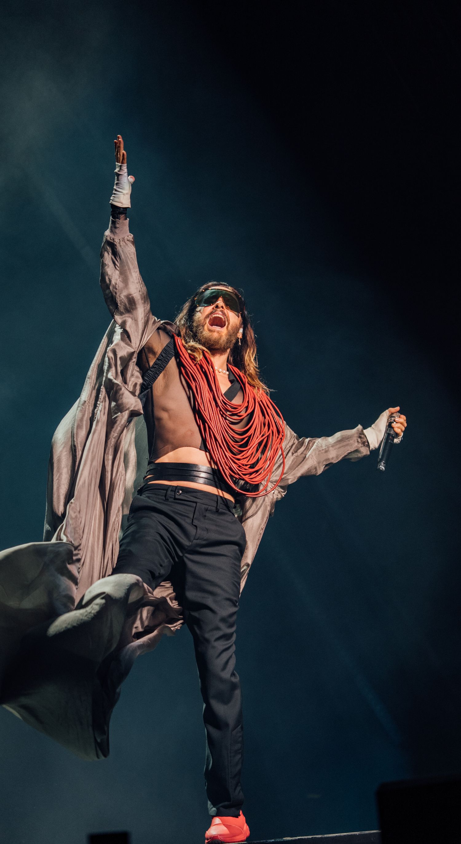 A performer in grey coat and red scarf strikes a dramatic pose on stage.