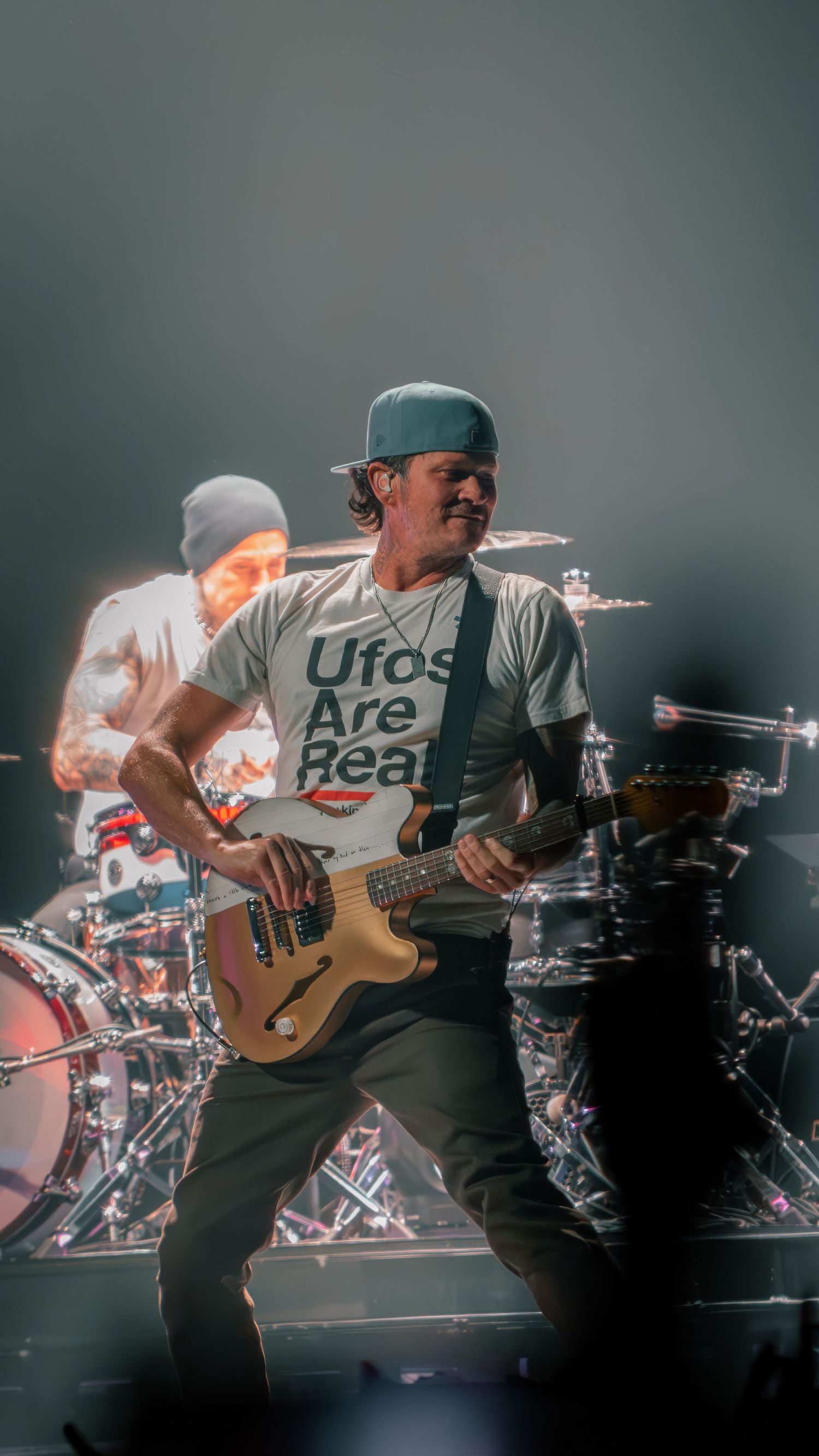Musicians performing on stage with guitars and drums during an energetic concert performance.