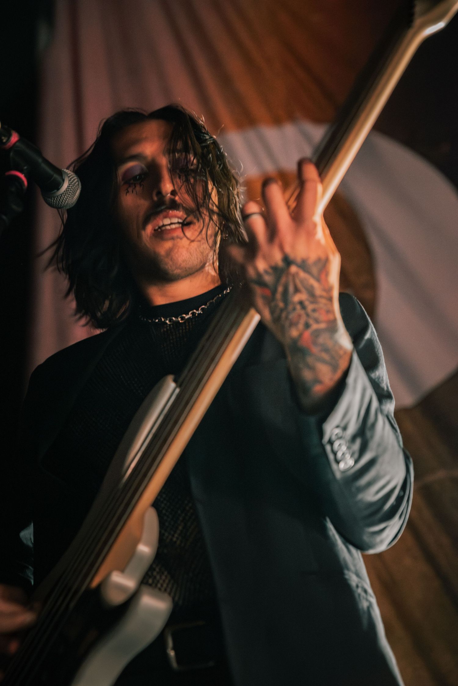 Tattooed musician performs passionately on bass guitar in dramatic concert lighting.