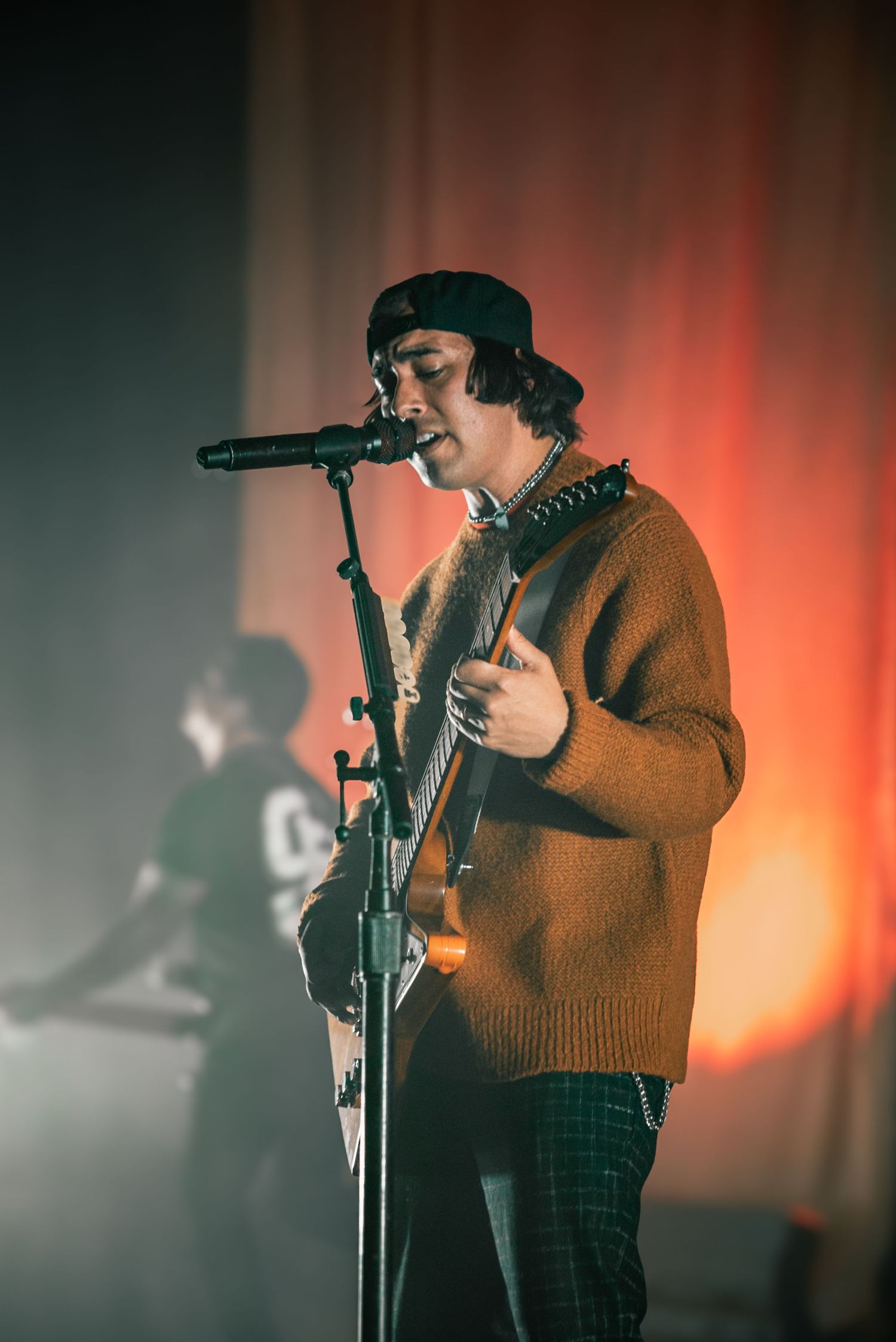 Musician performs on stage with dramatic red backlighting and foggy atmosphere.