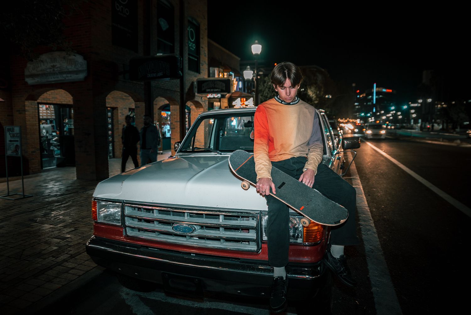 Vintage pickup truck parked on dark street with illuminated buildings in background.