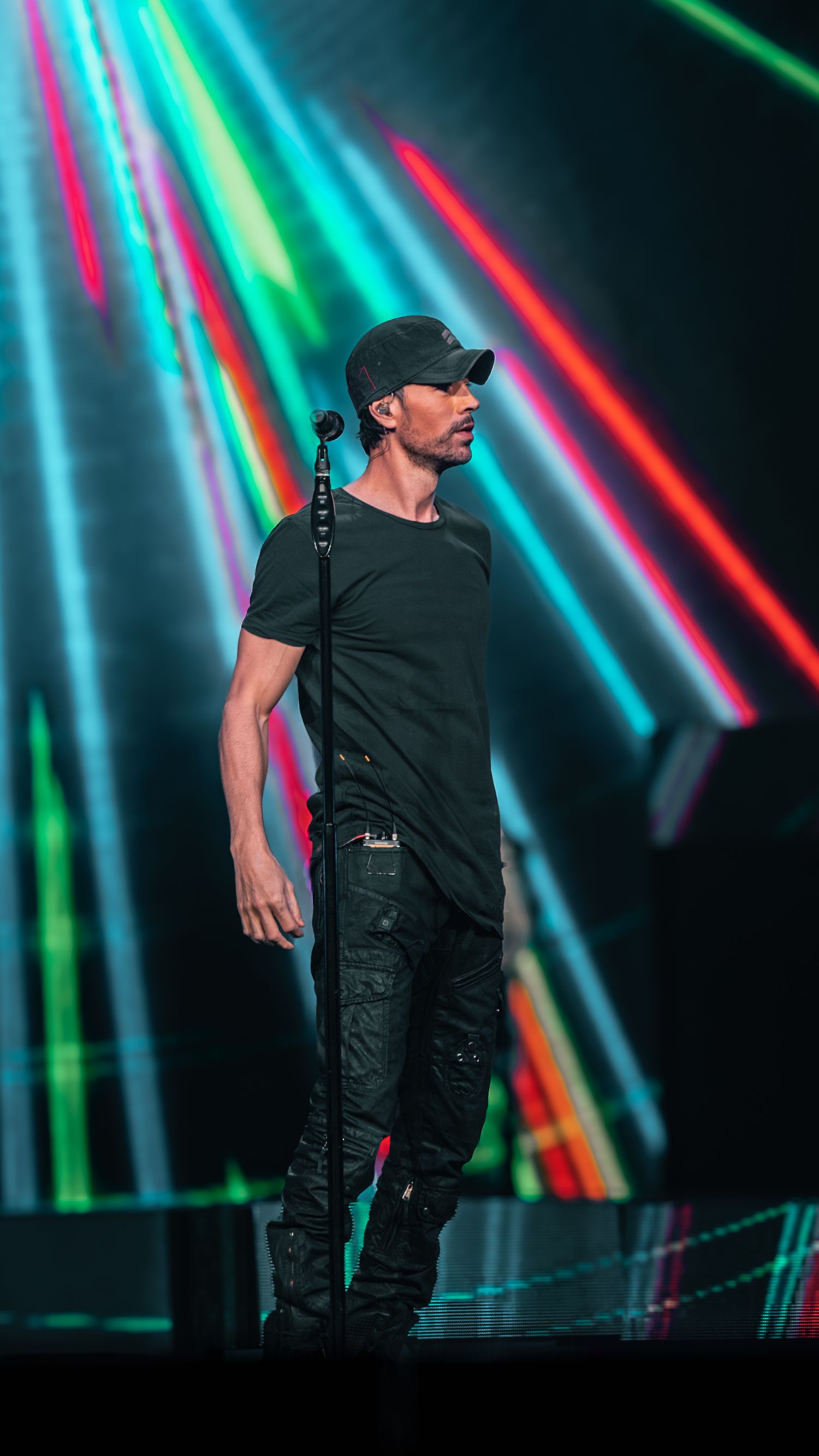 Performer on stage with colorful neon light beams creating dramatic backdrop during concert.