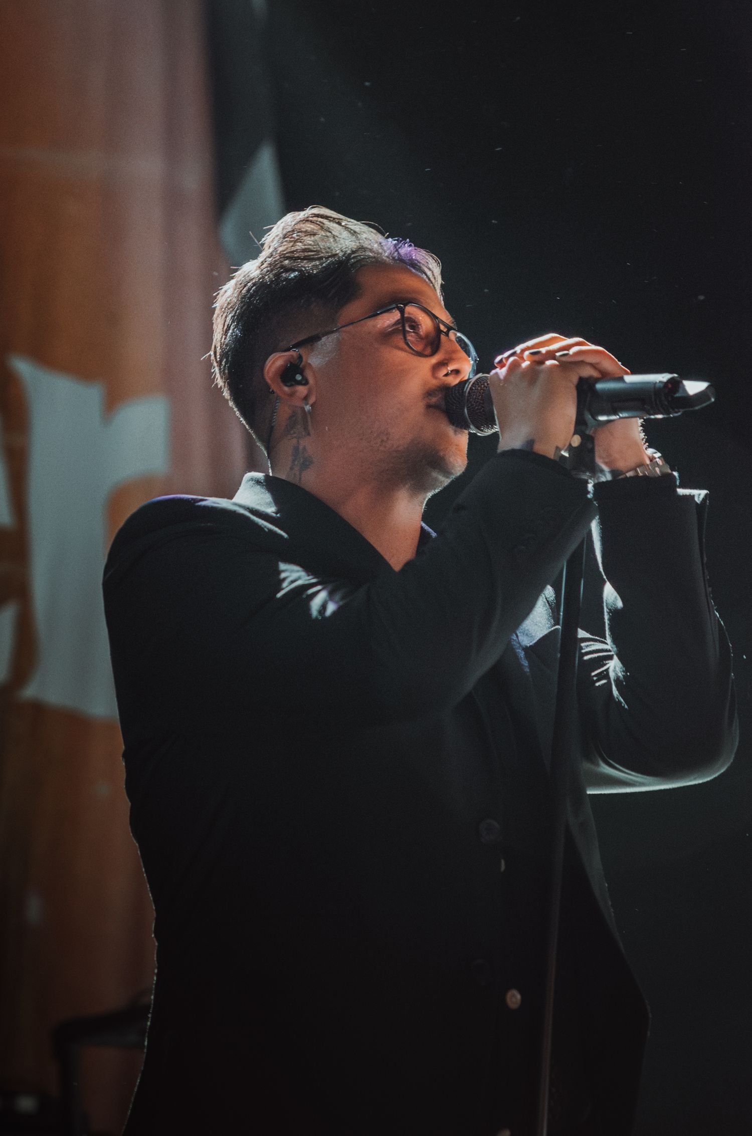 Vocalist performs in black attire with dramatic stage lighting and microphone.