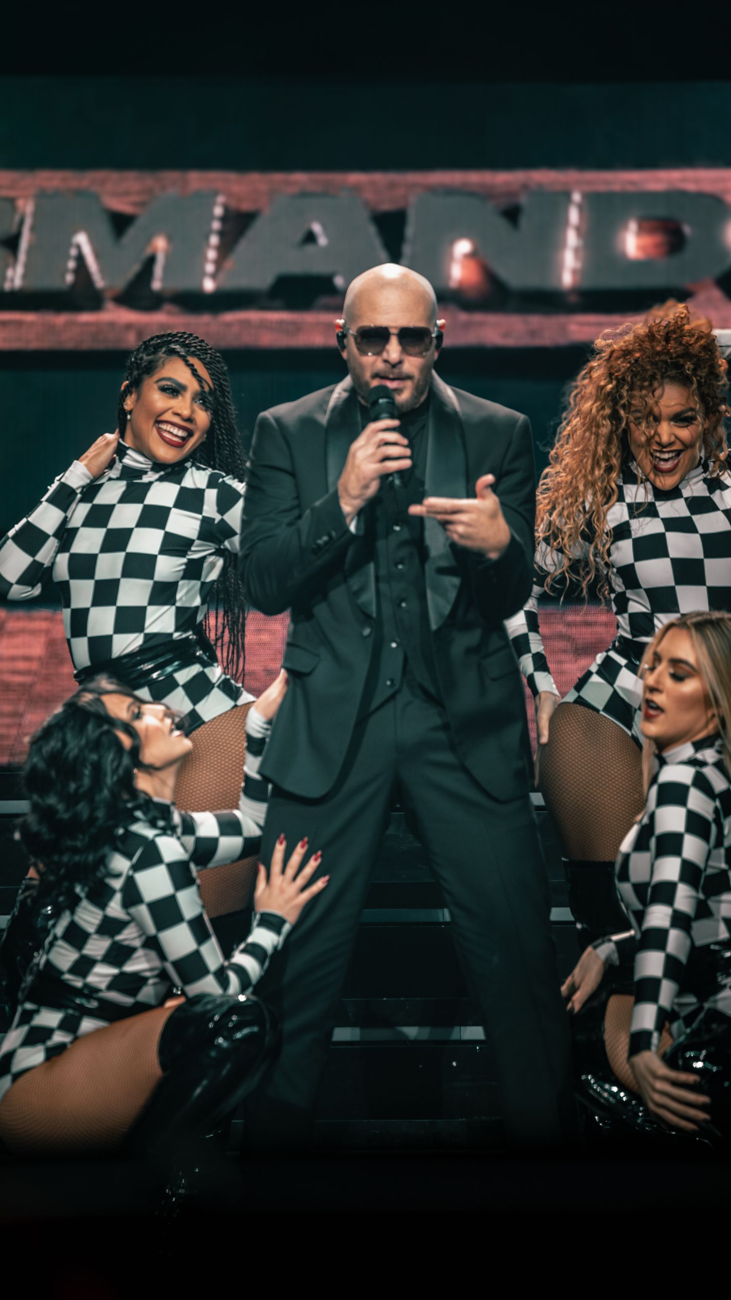 Dynamic stage show featuring performers in checkerboard outfits against red illuminated backdrop.