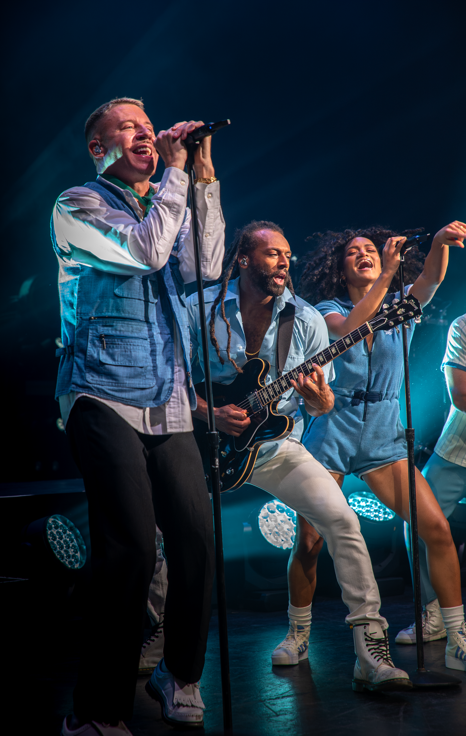 Group of performers in coordinated outfits singing together on a concert stage.