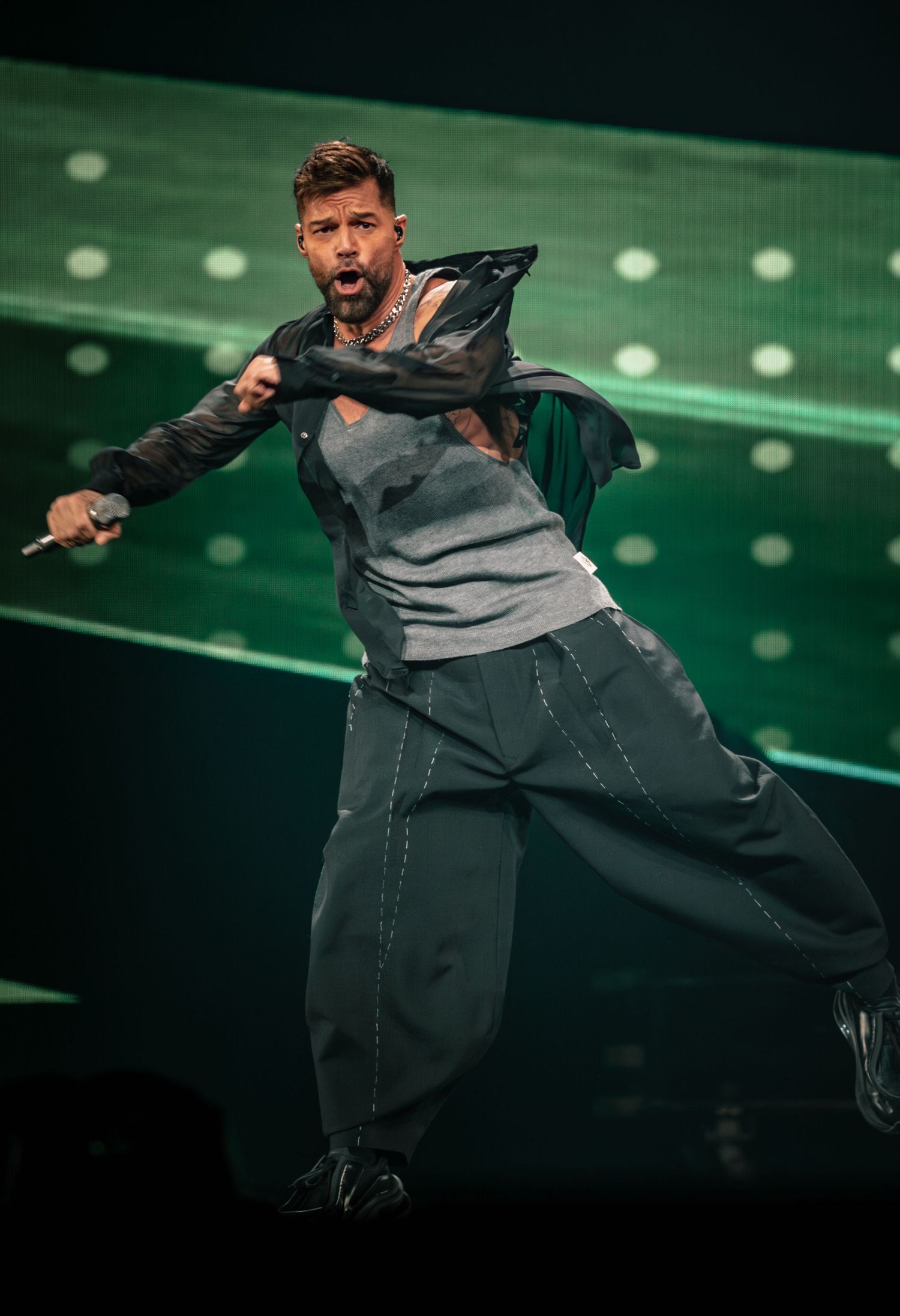 Artist in black and gray outfit dancing energetically on green-lit stage.