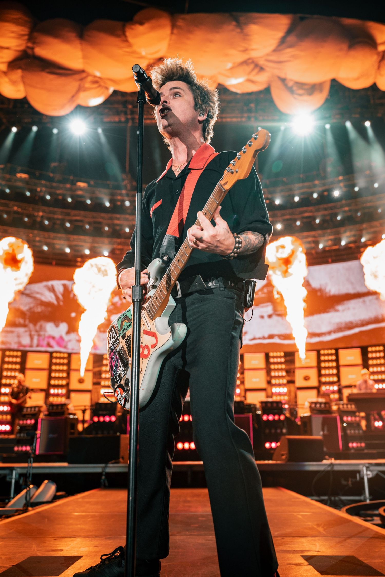 Rock performance on stage with dramatic orange lighting and pyrotechnic fire effects.
