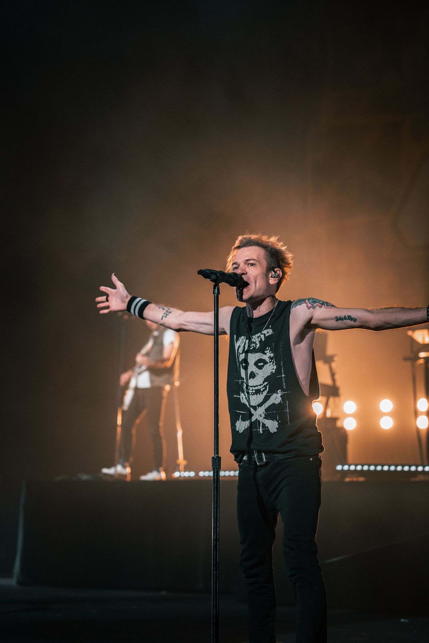 Rock performer sings passionately on stage with arms outstretched during concert performance.