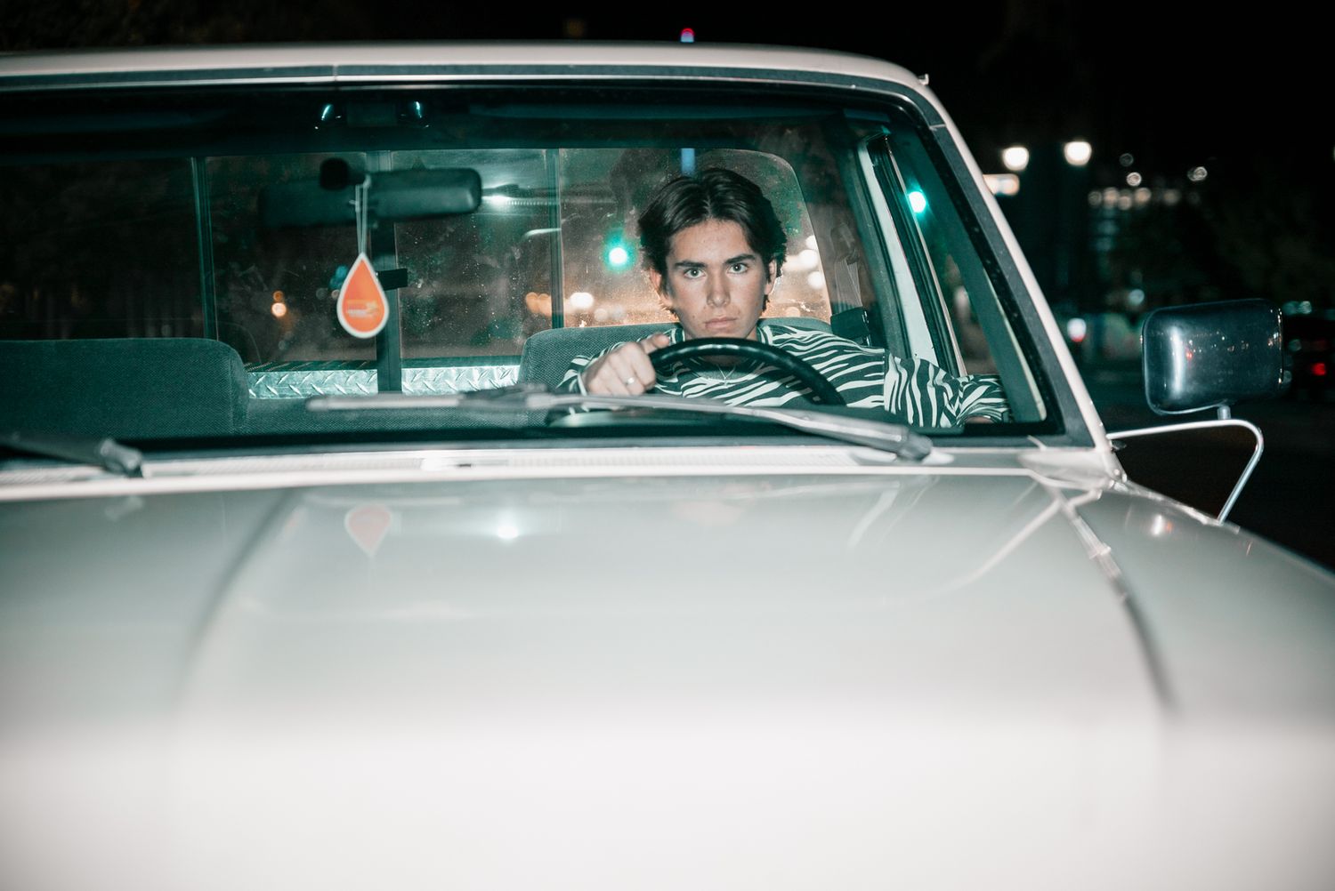 Close-up shot through windshield of classic car at night with city lights.