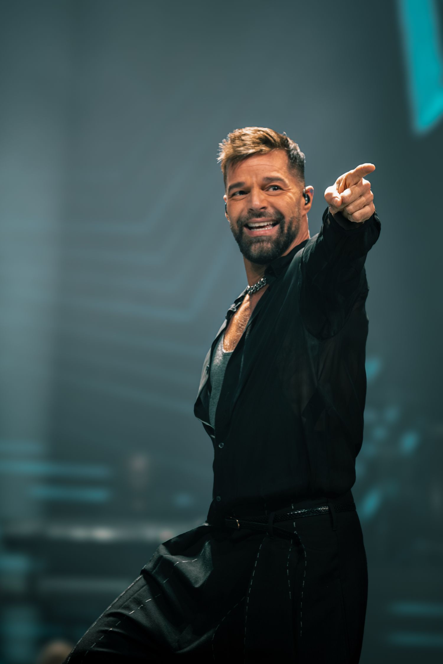 Singer in black outfit performing energetically on stage with raised arms.