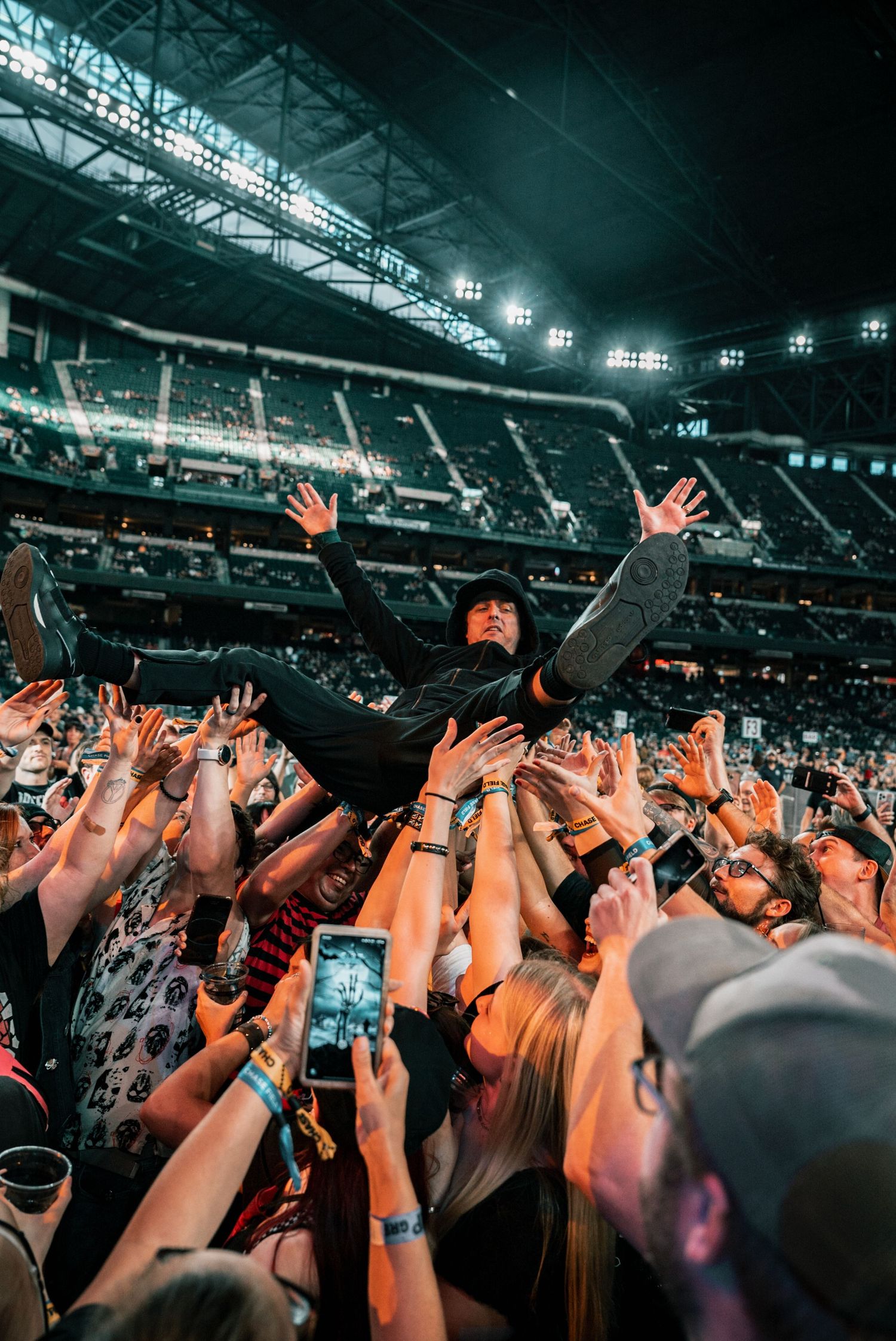 Crowd surfer floats above audience hands during indoor arena concert.