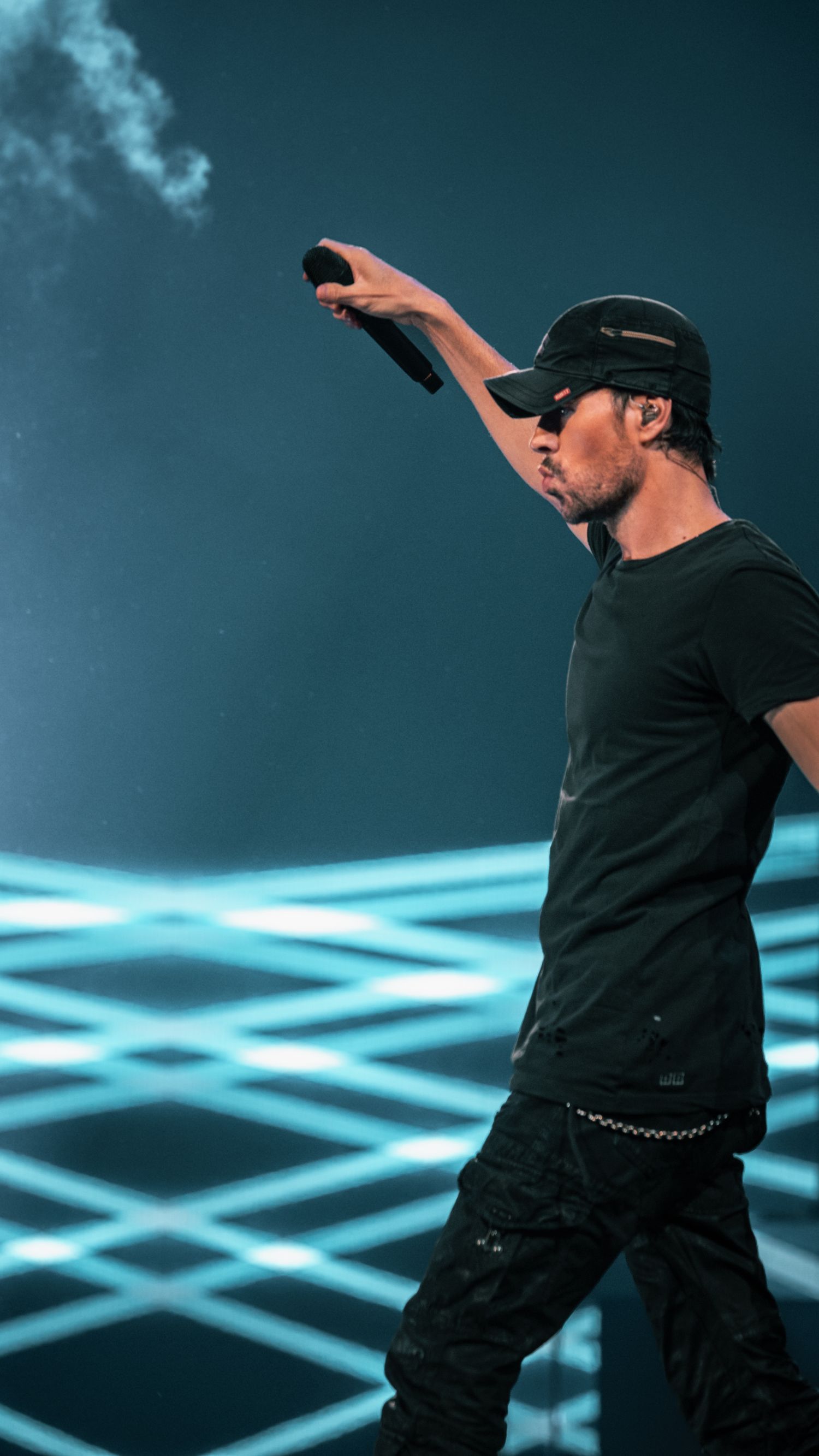 Singer in black attire performing against geometric blue light pattern background.