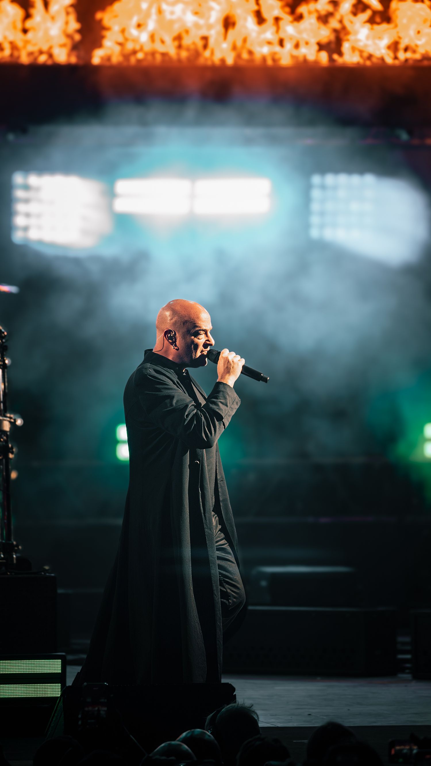 Performer in black outfit singing on stage with dramatic lighting and smoke effects.