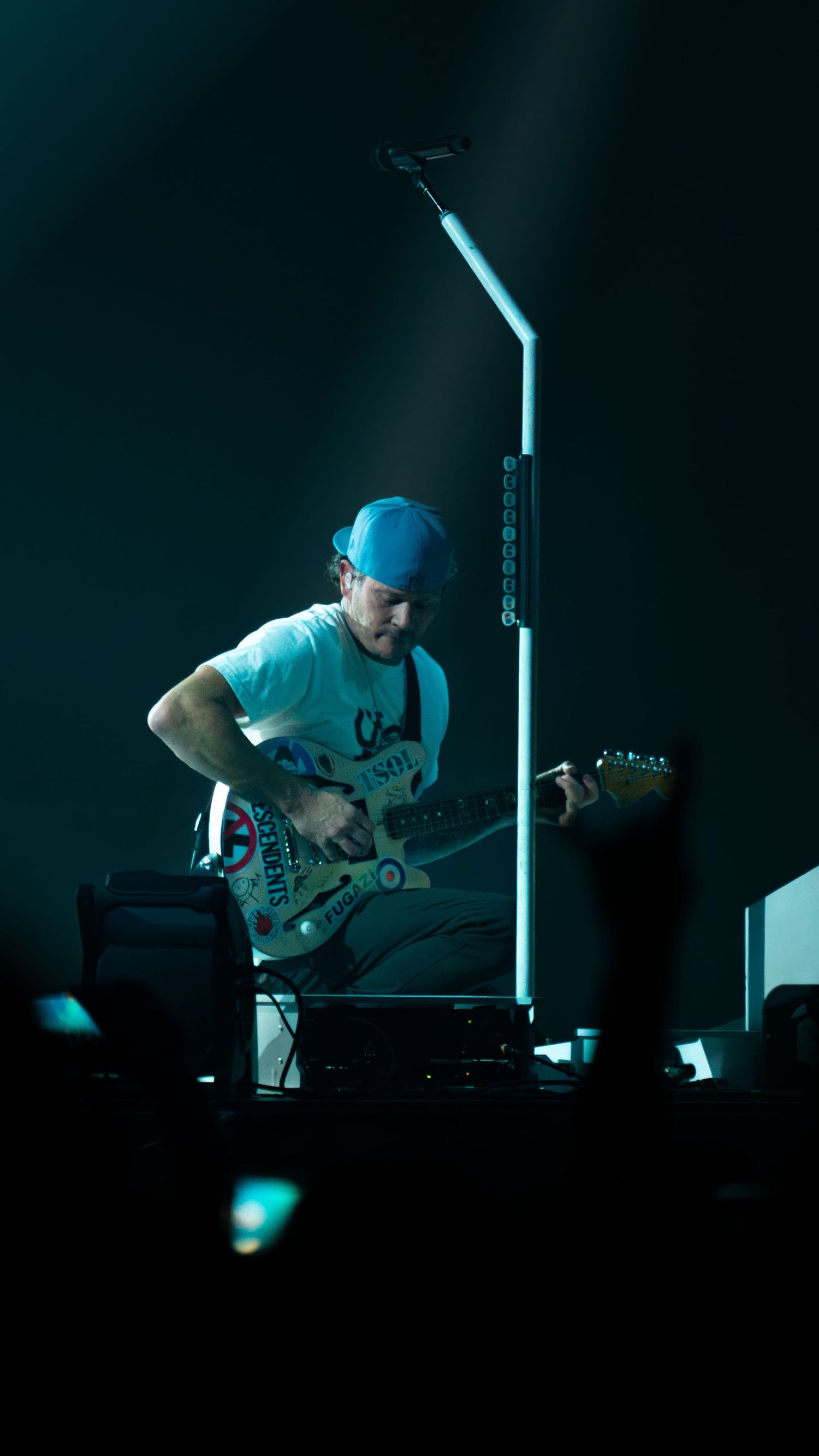 Concert performer plays keyboard instrument in dramatic blue lighting on darkened stage.