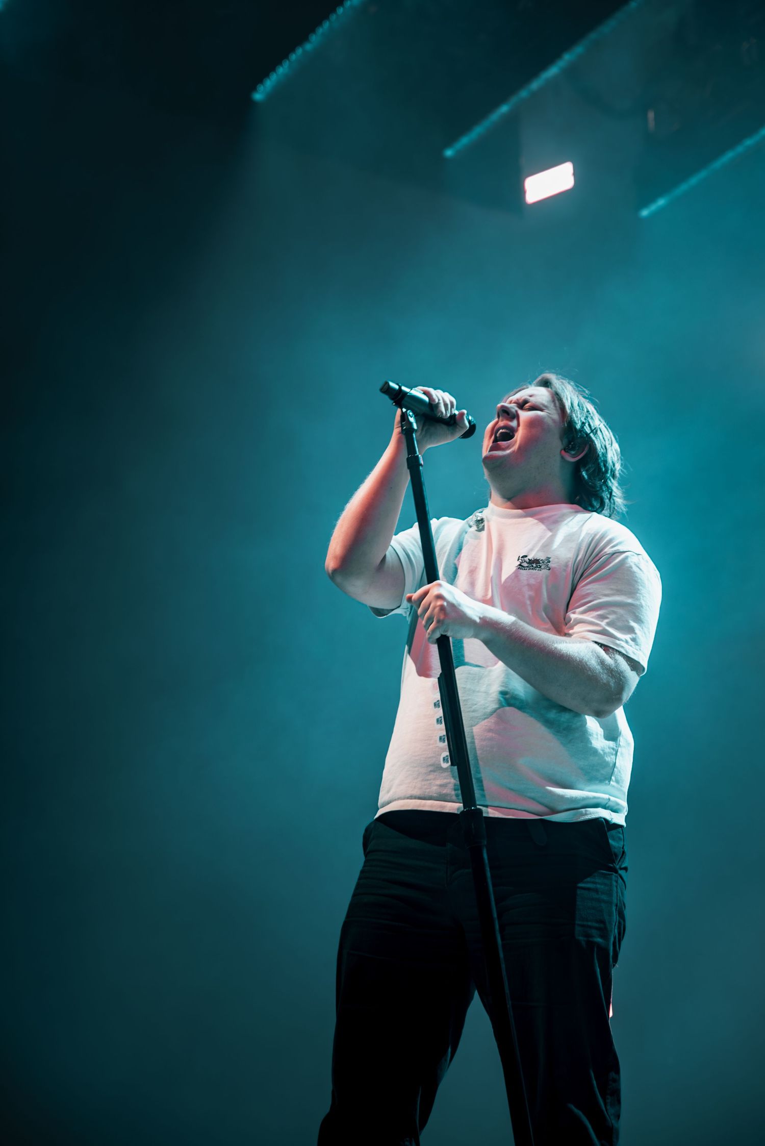 Performer in white t-shirt delivers passionate vocals against moody blue stage lighting.