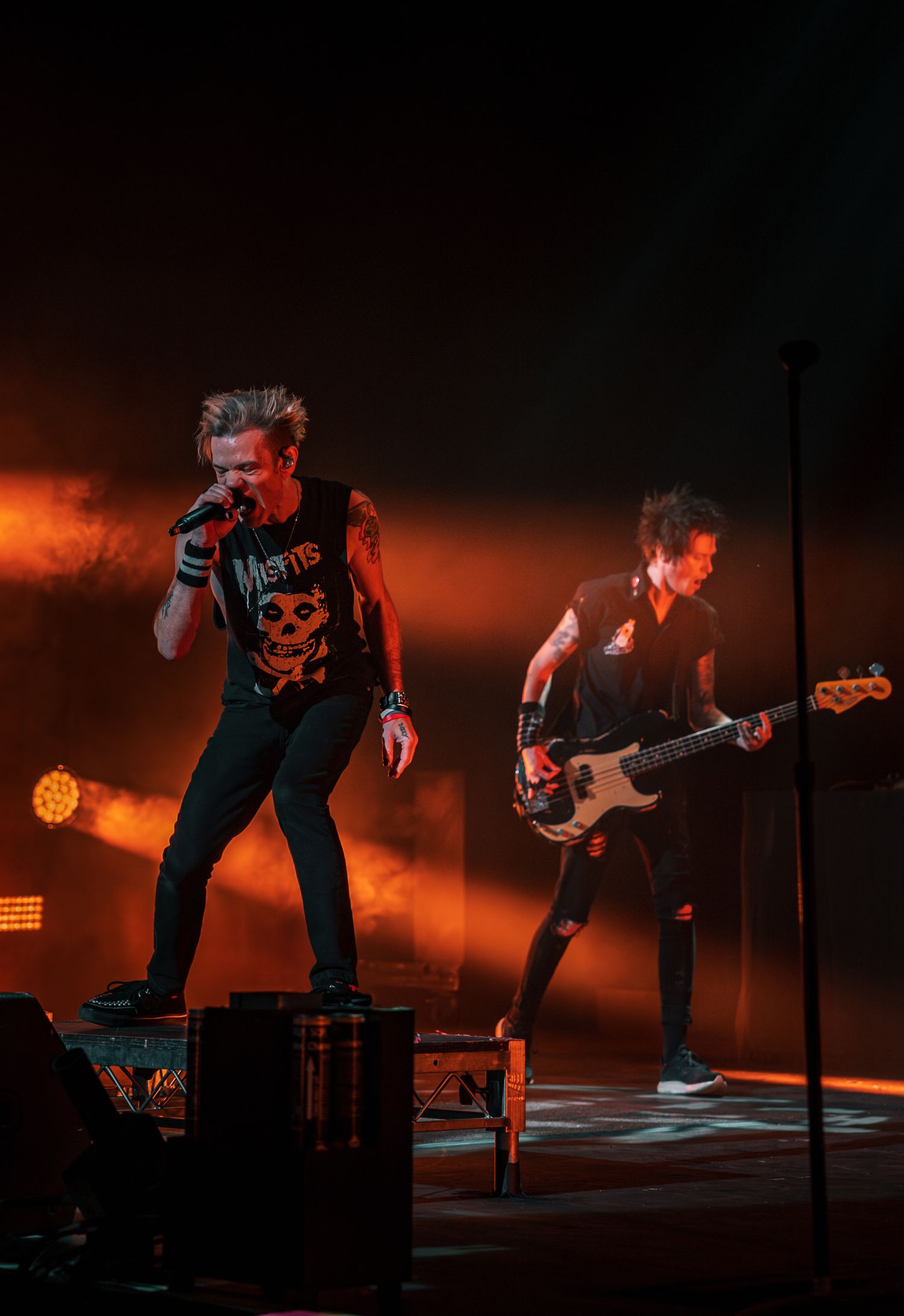 Rock musicians perform energetically on stage with dramatic orange lighting and smoke effects during a concert.