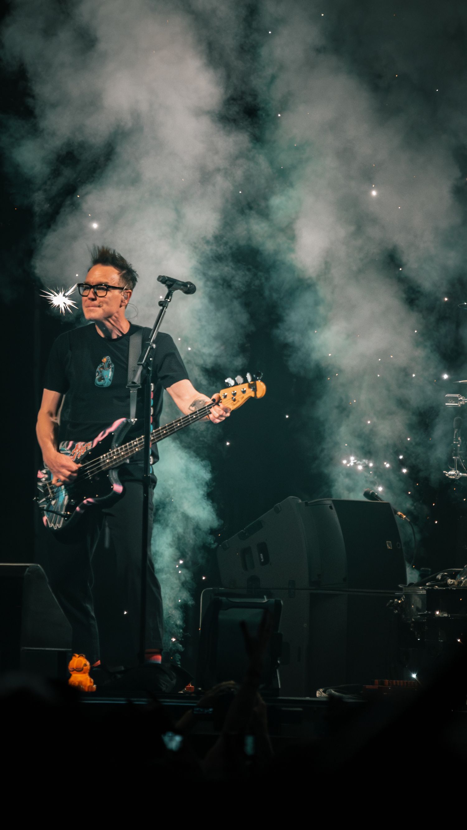 Rock band performs on smoky stage with dramatic lighting effects and crowd in background.
