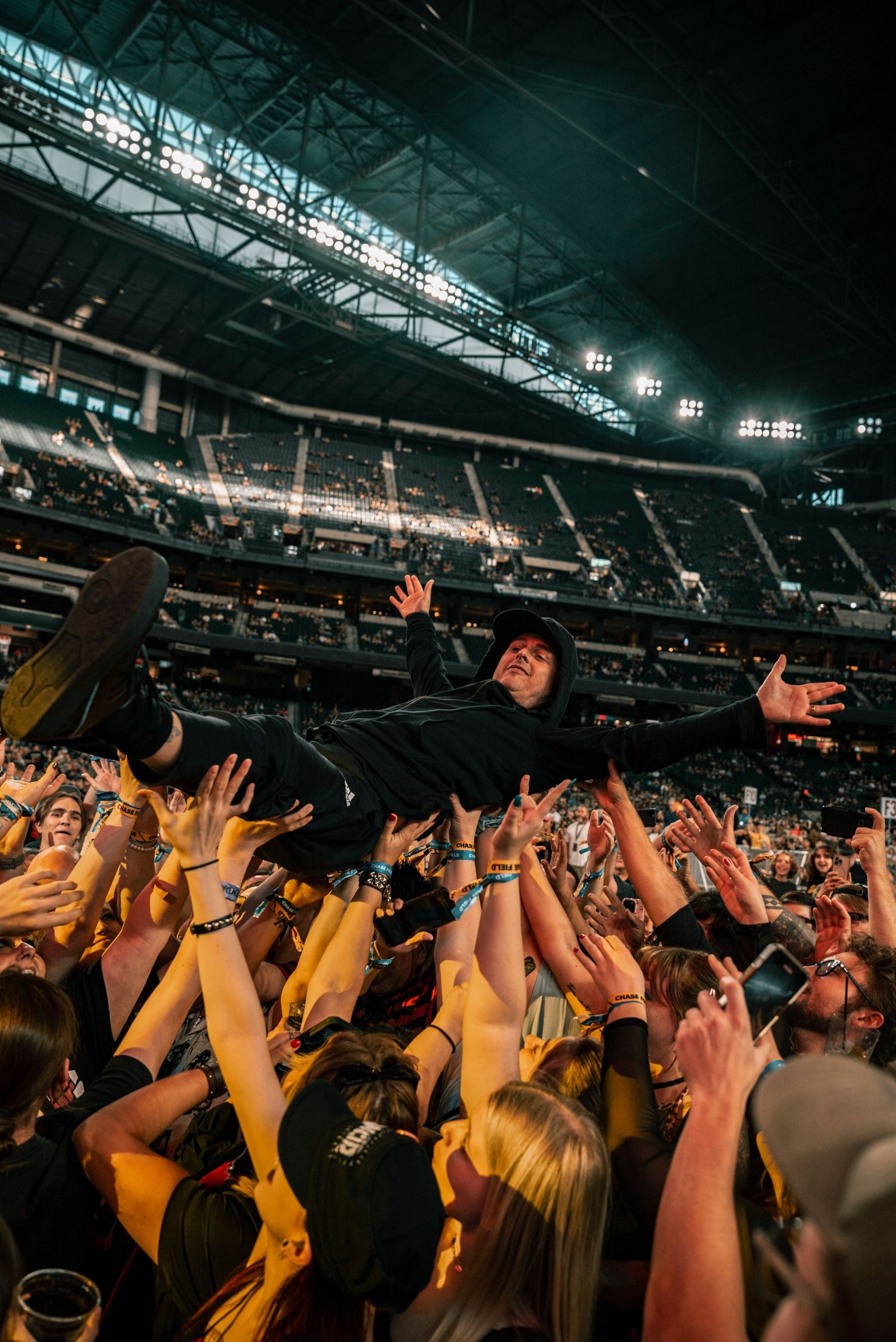 Musician crowd surfs above enthusiastic fans at indoor arena show.