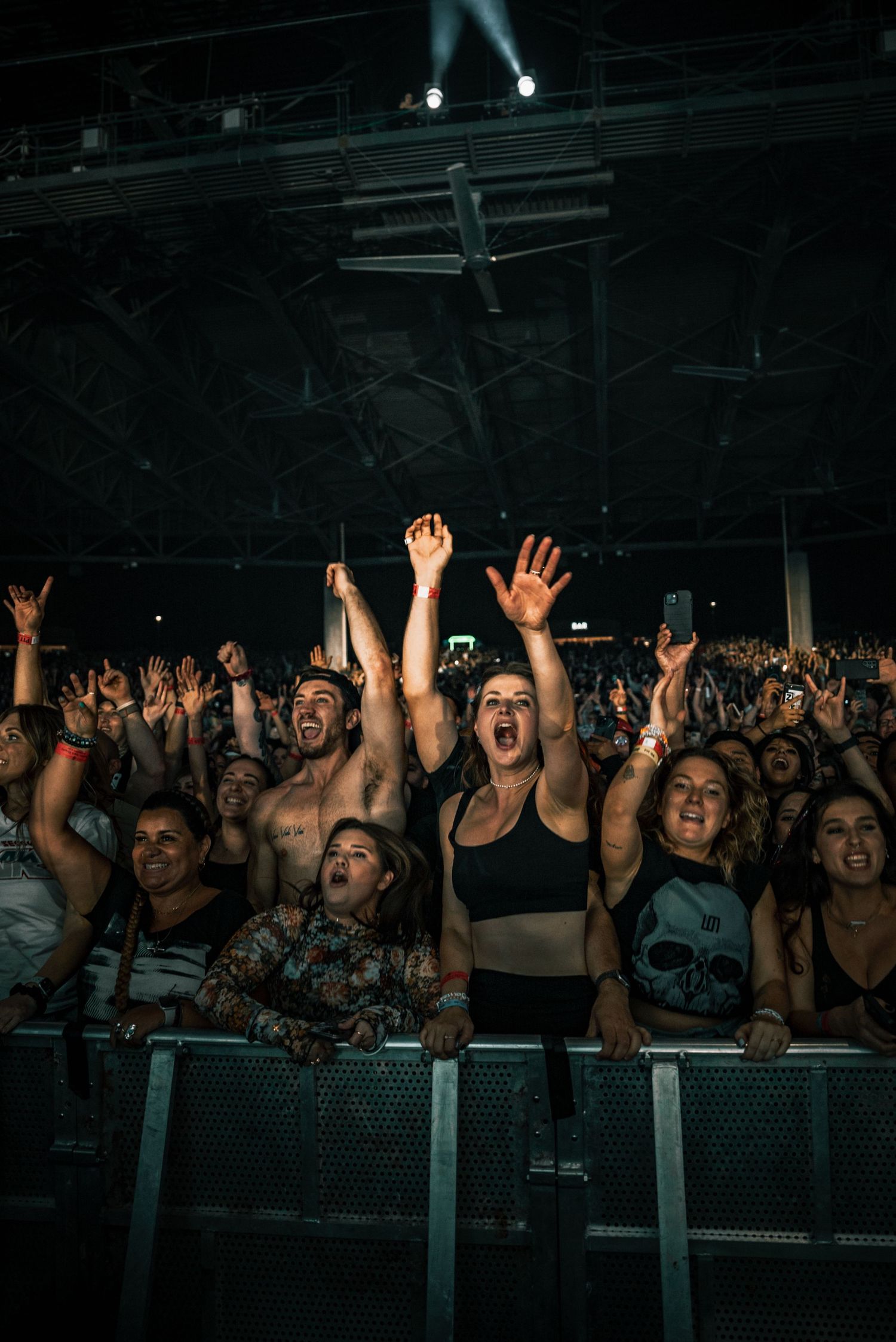 An enthusiastic concert crowd with raised hands cheering at a dark indoor venue.