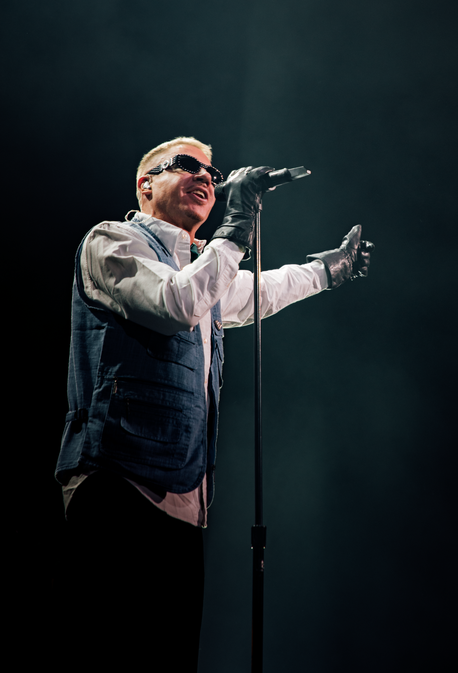 Dramatic stage performance with artist in white vest gesturing against dark background.
