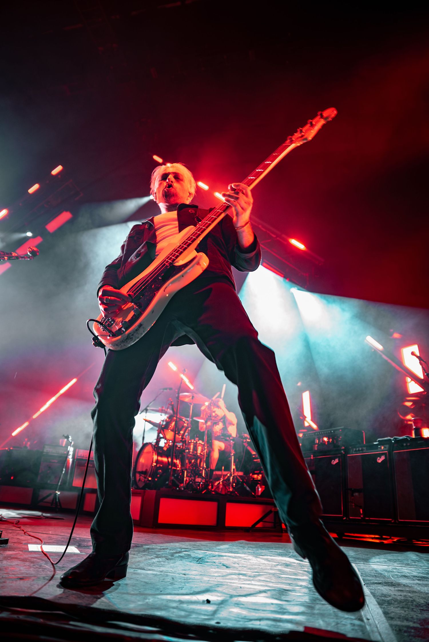 Rock performer plays guitar on stage bathed in dramatic red lighting during intense concert moment.