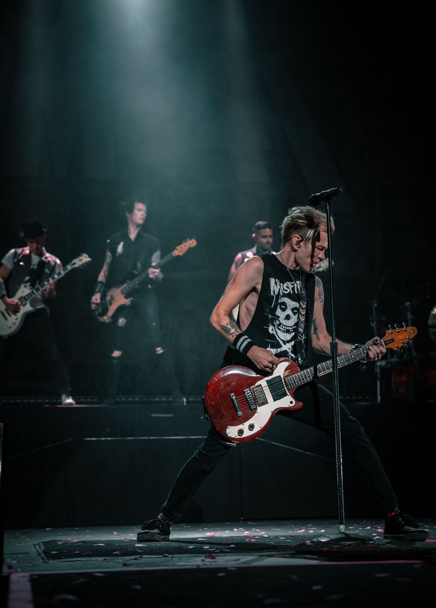 Rock musician plays electric guitar while performing on dimly lit concert stage.