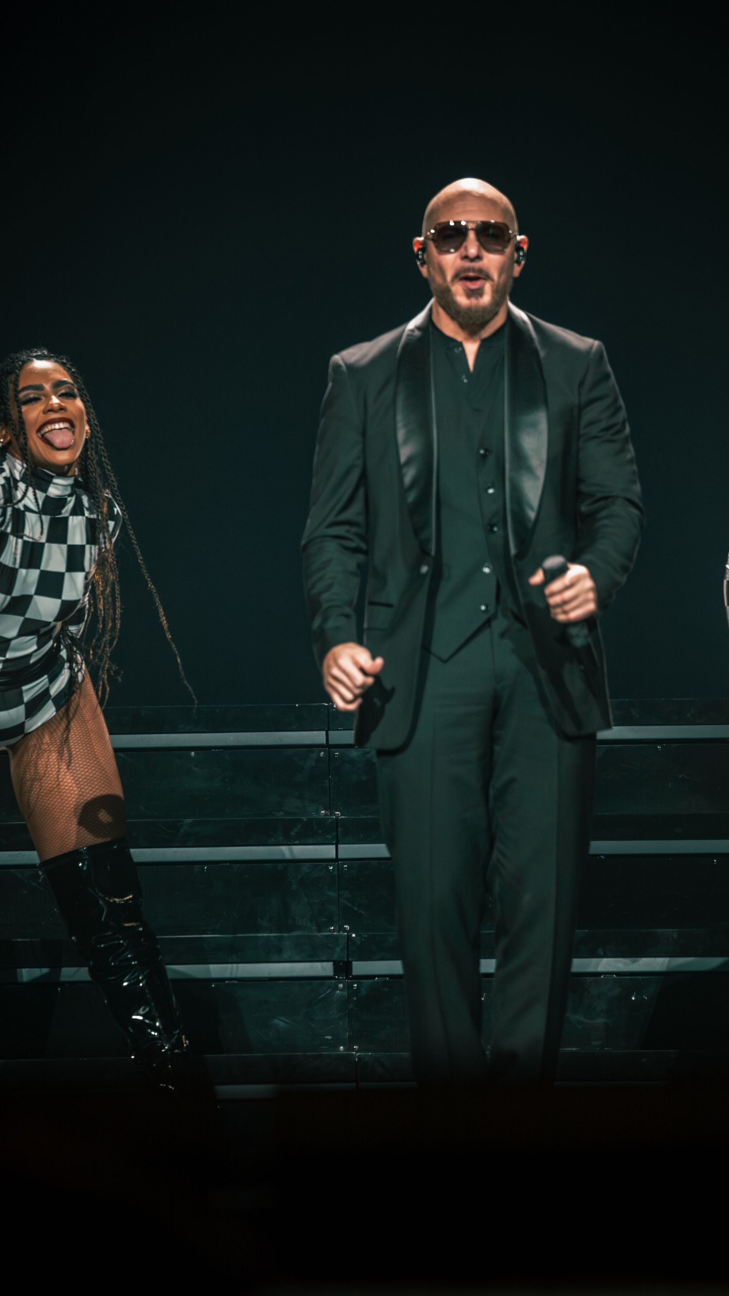 Dynamic performers in black suits and checkered outfits energetically dance on dark stage.