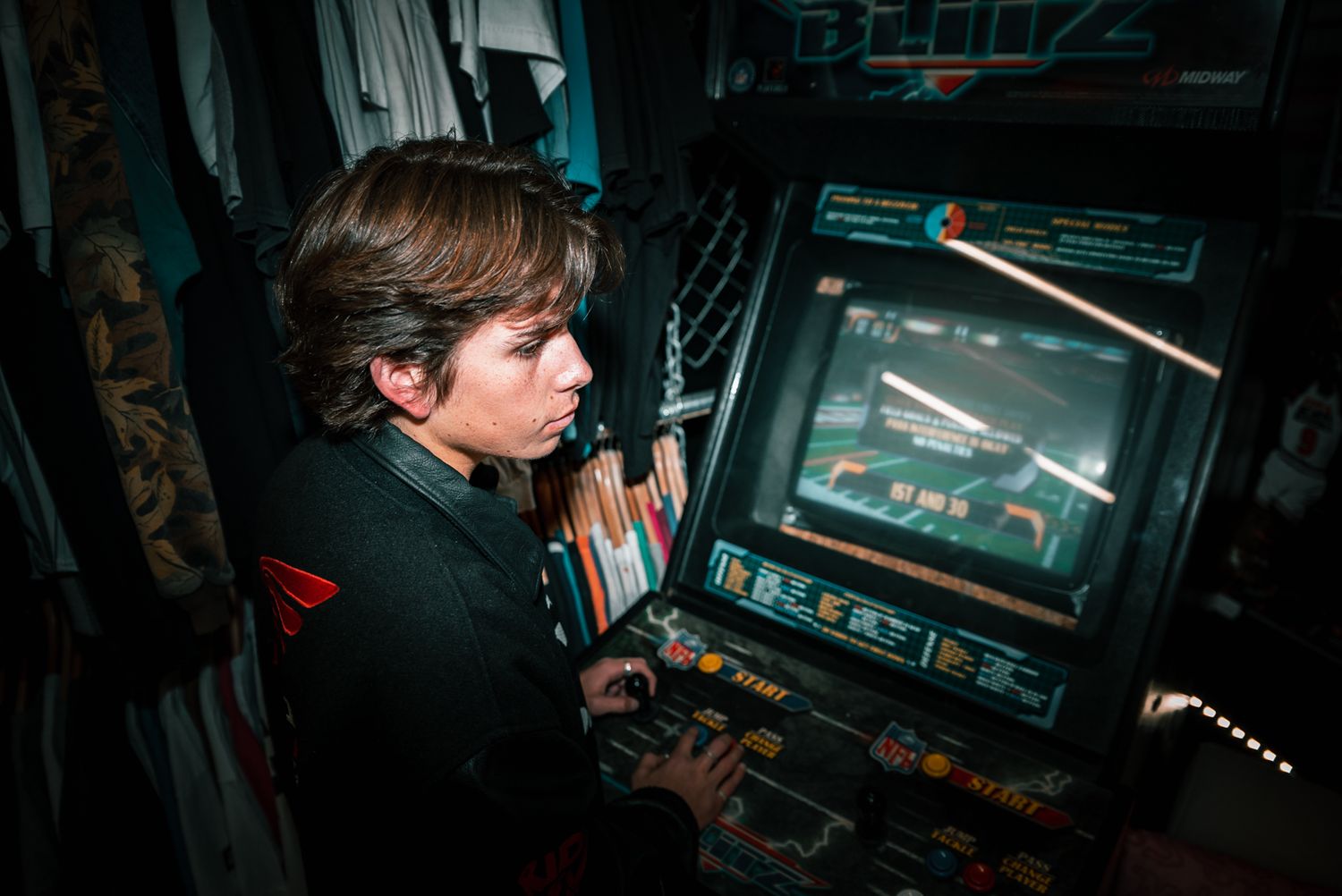 Person playing arcade game in dimly lit room with vintage gaming cabinet.