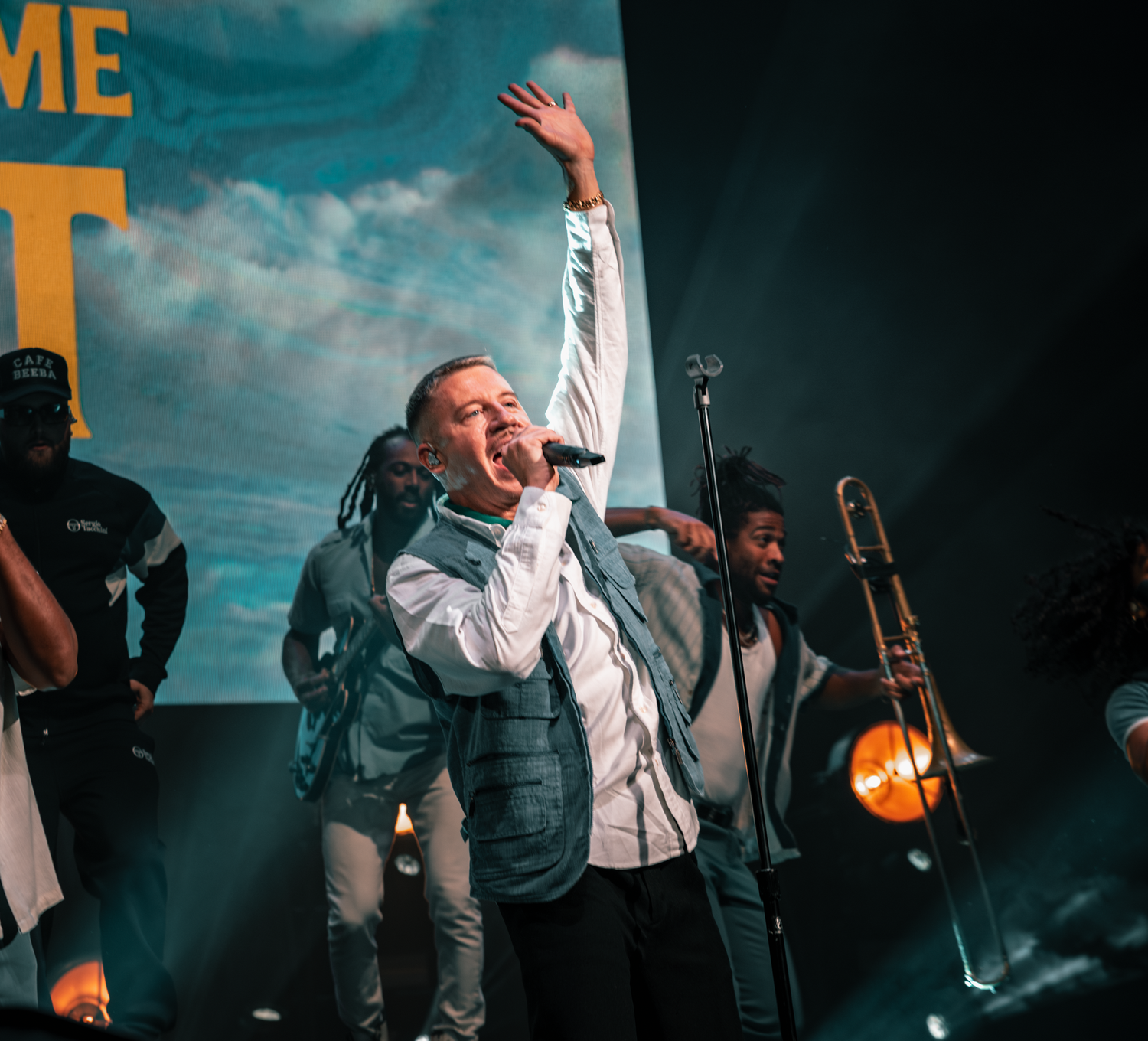 Band members performing on stage with dramatic turquoise lighting and atmospheric effects.