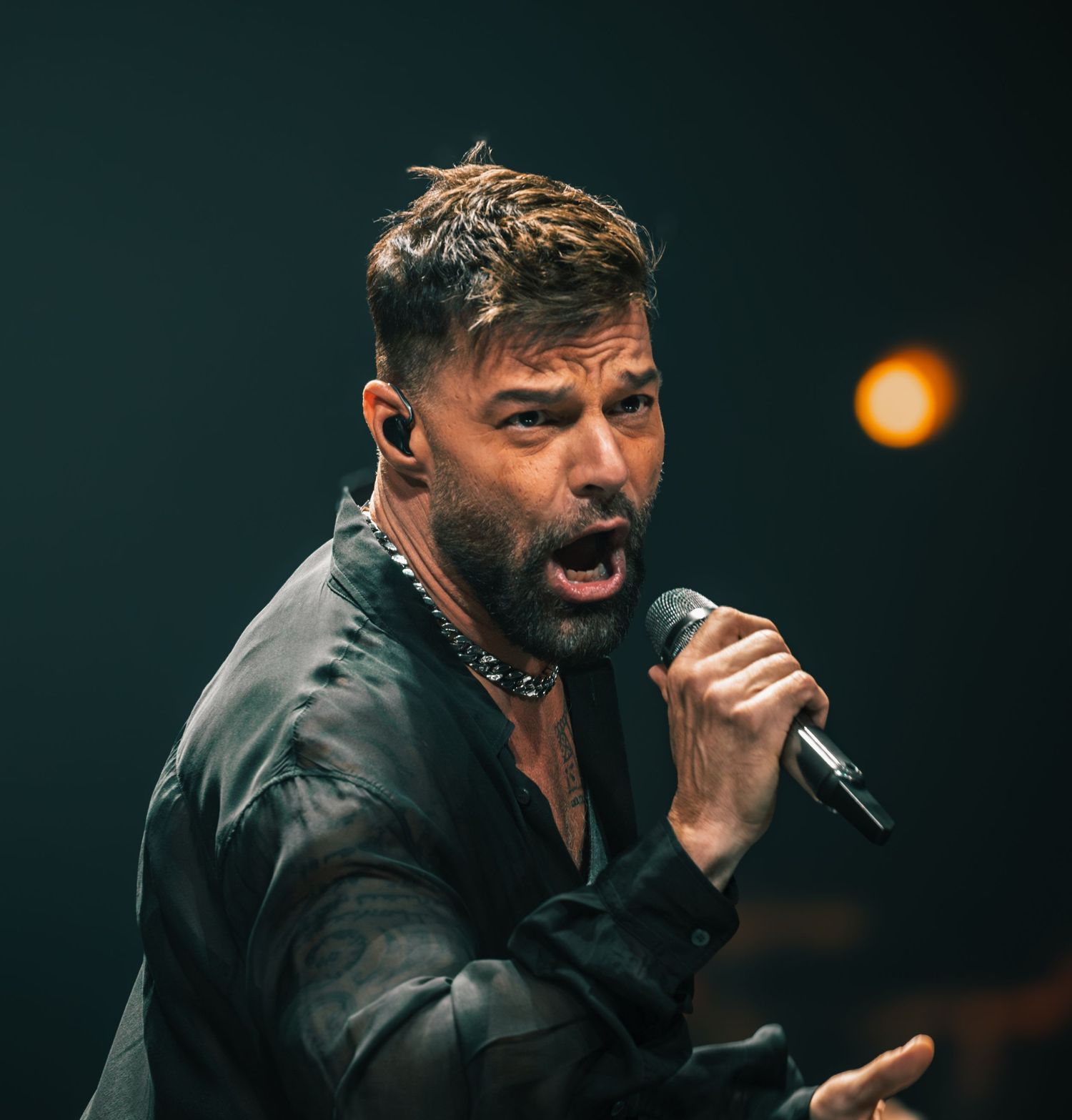 Performer in black jacket singing passionately into microphone during concert.