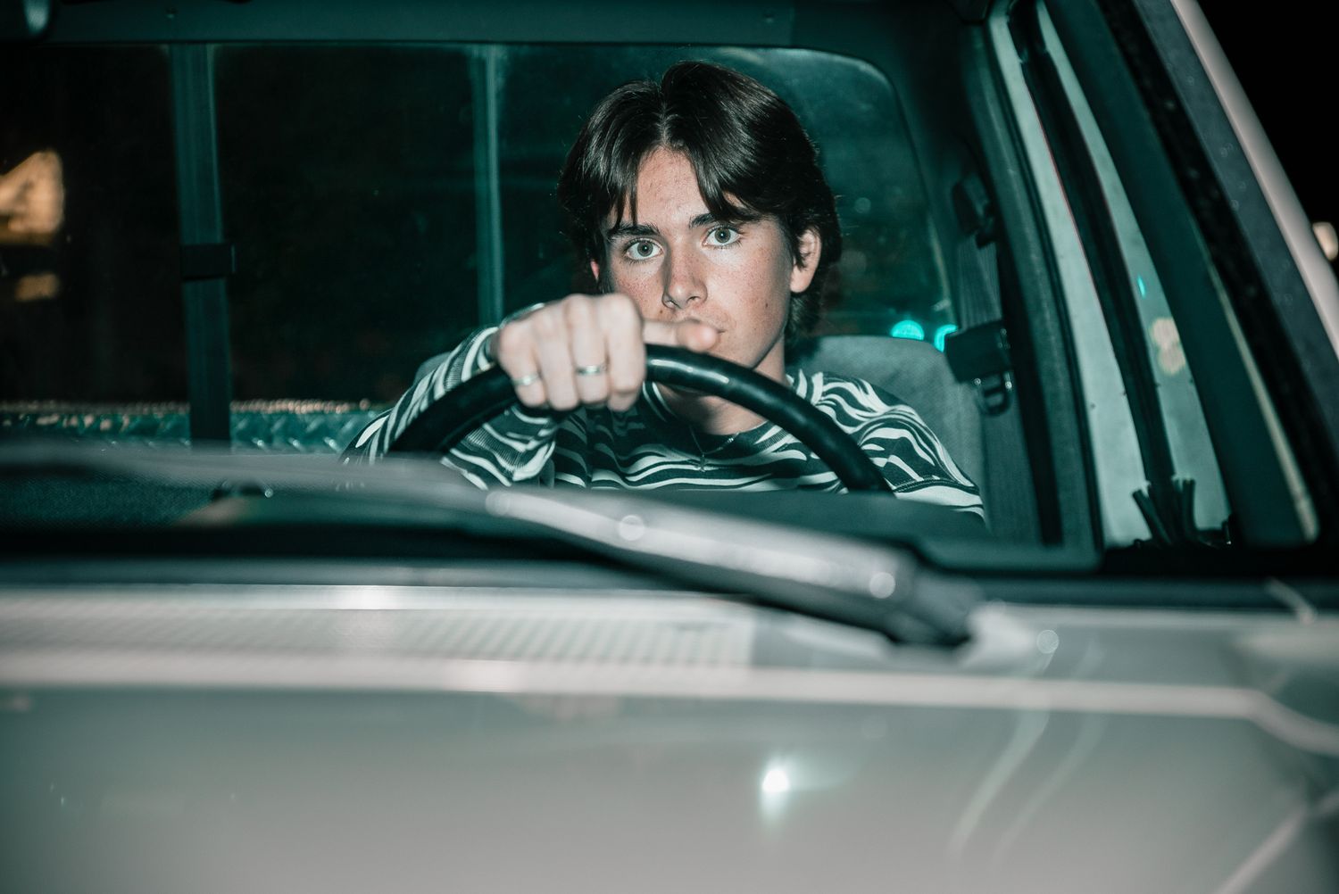Nighttime portrait through a car window with moody green lighting.