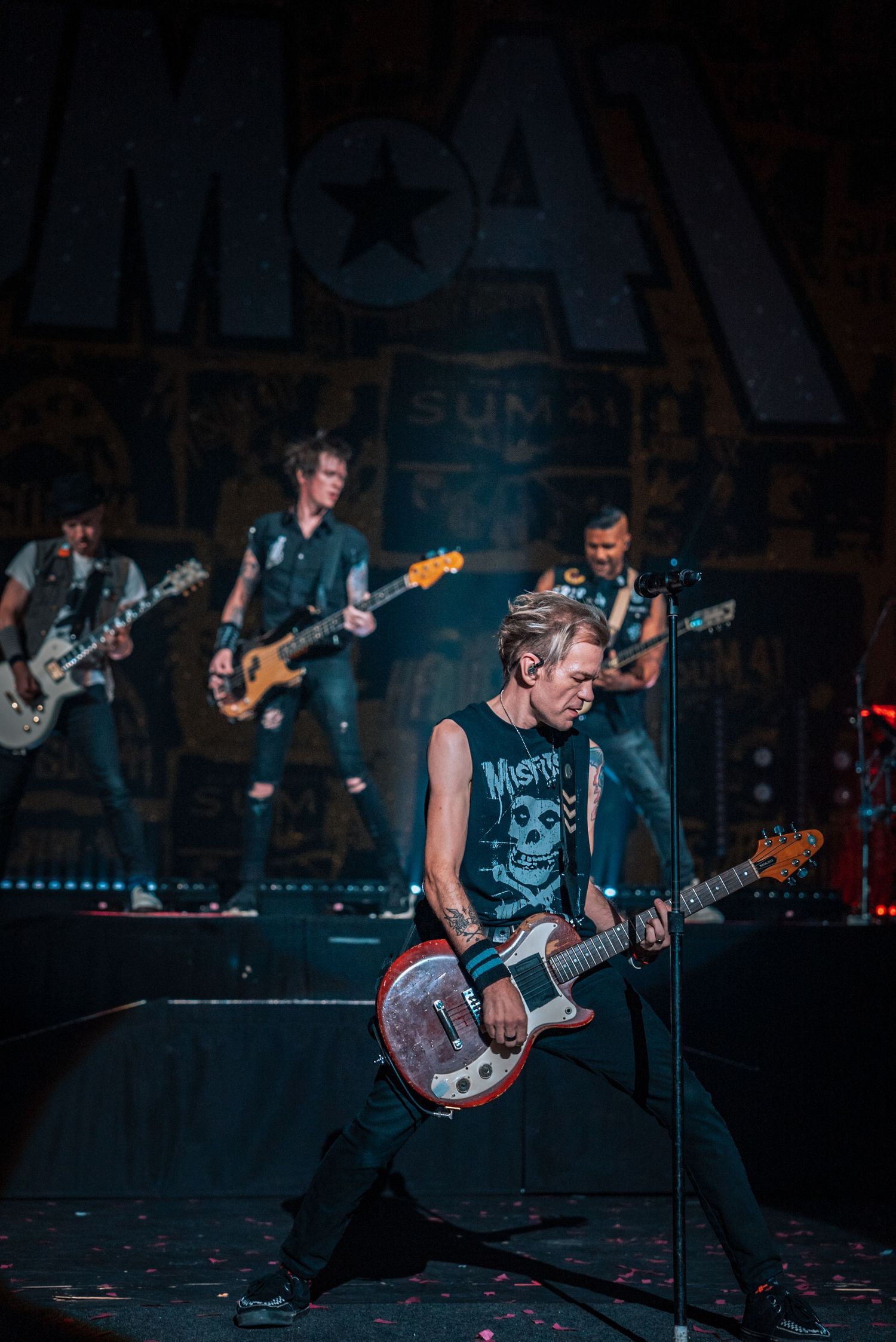 Rock band performs on stage with dramatic lighting and backdrop.