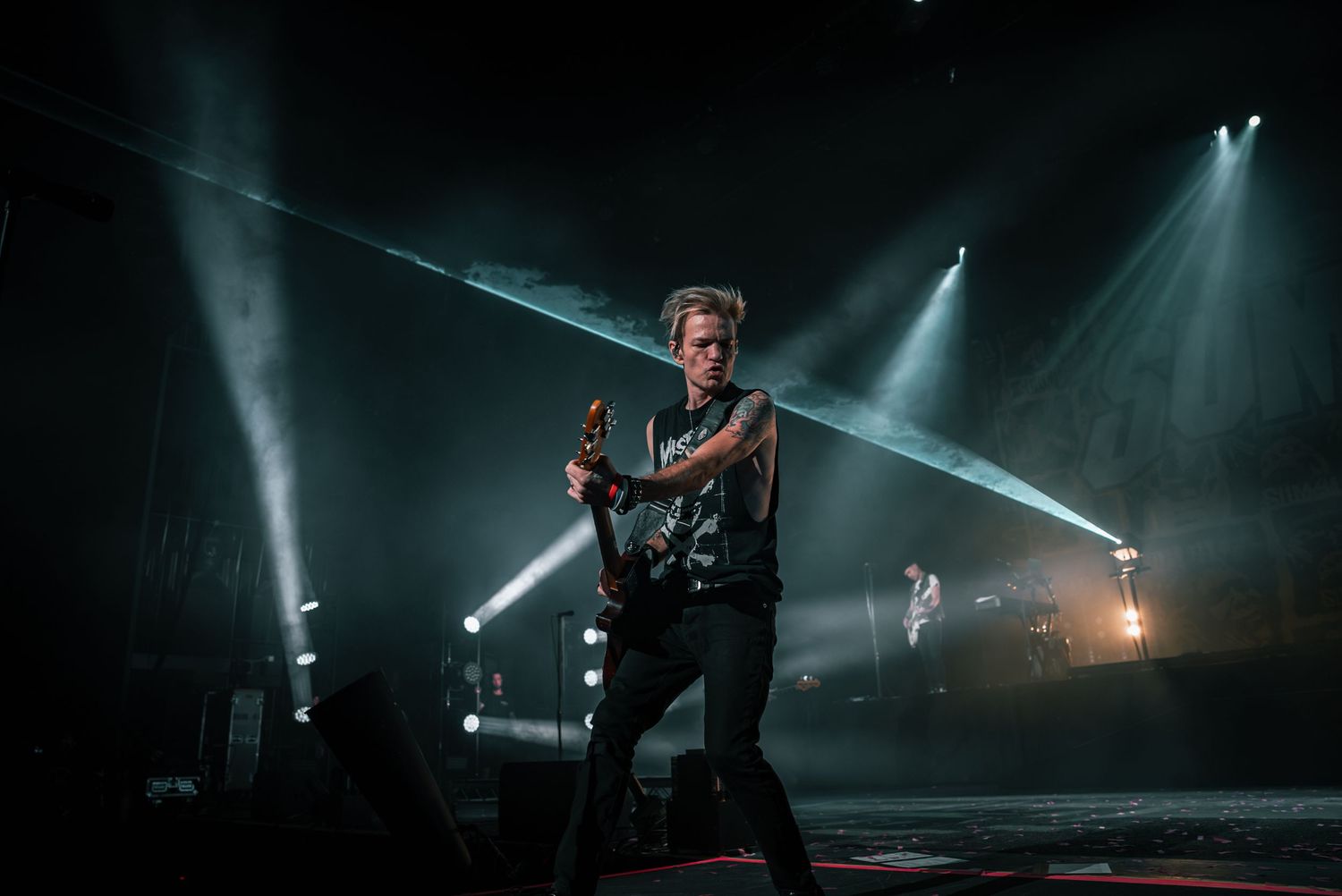 Concert stage illuminated by dramatic white spotlights during performance.