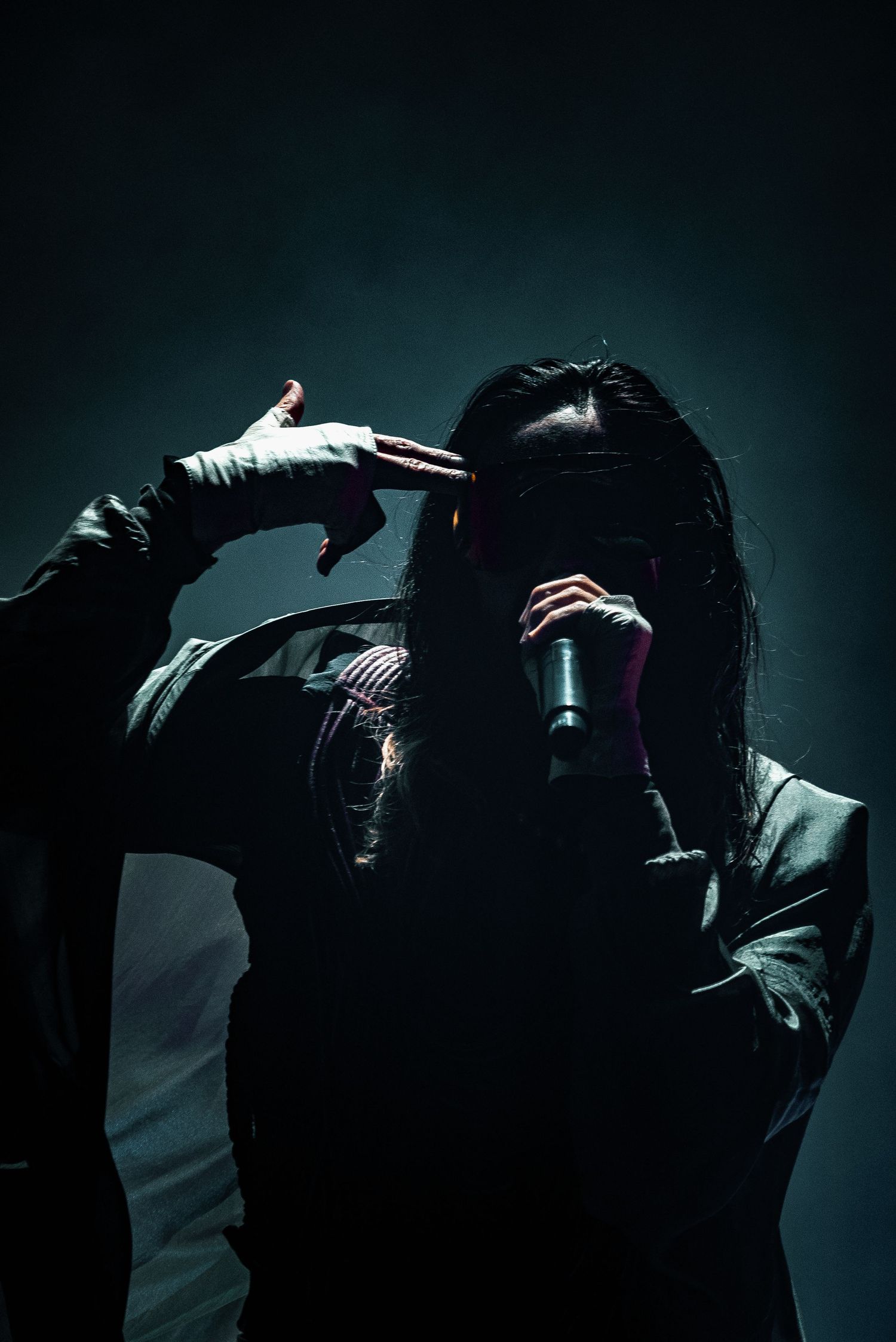 Dramatic silhouetted performer singing into microphone against dark background.