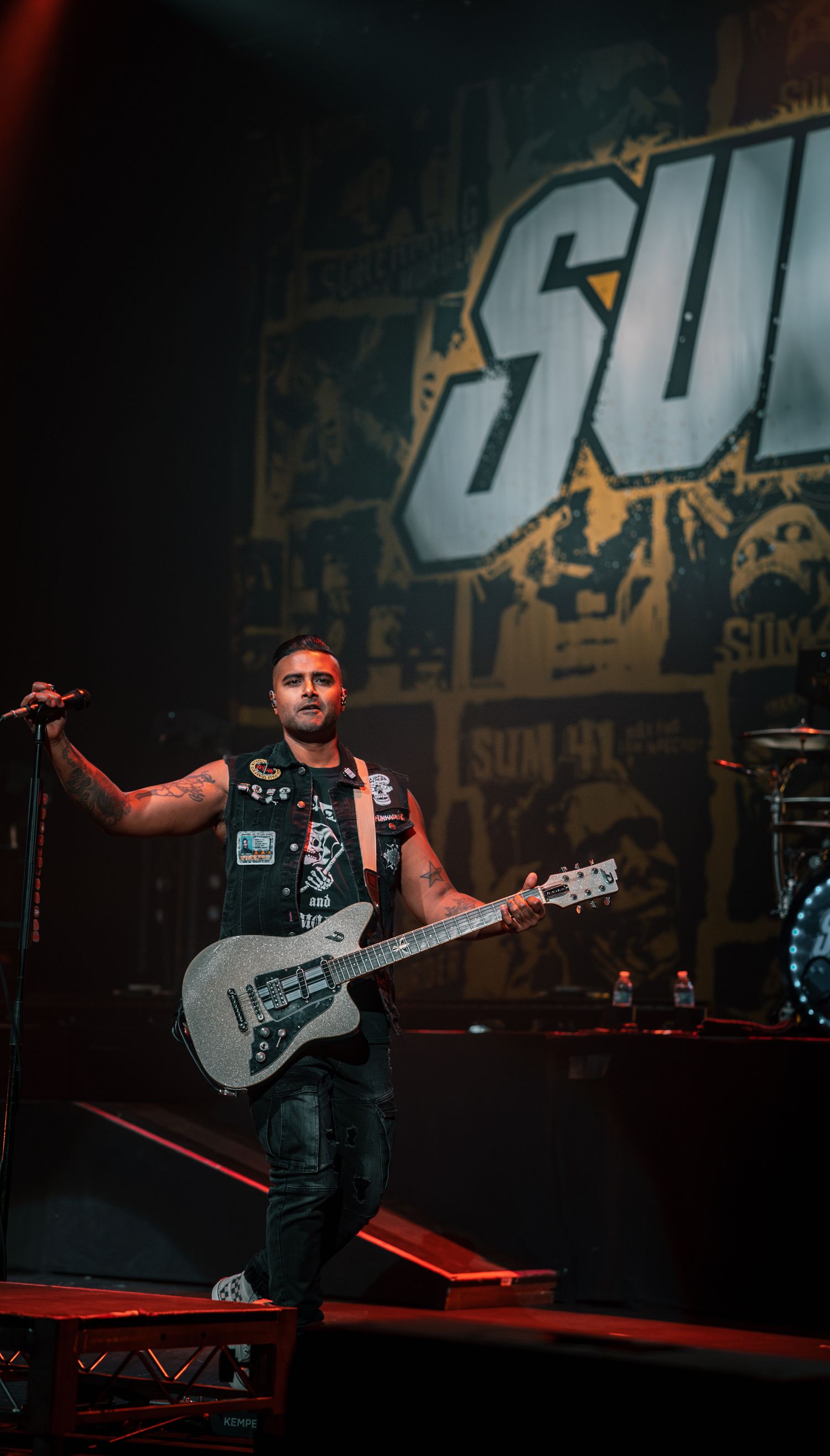 Musician plays guitar on stage with large 'SUM' text backdrop and dramatic lighting.