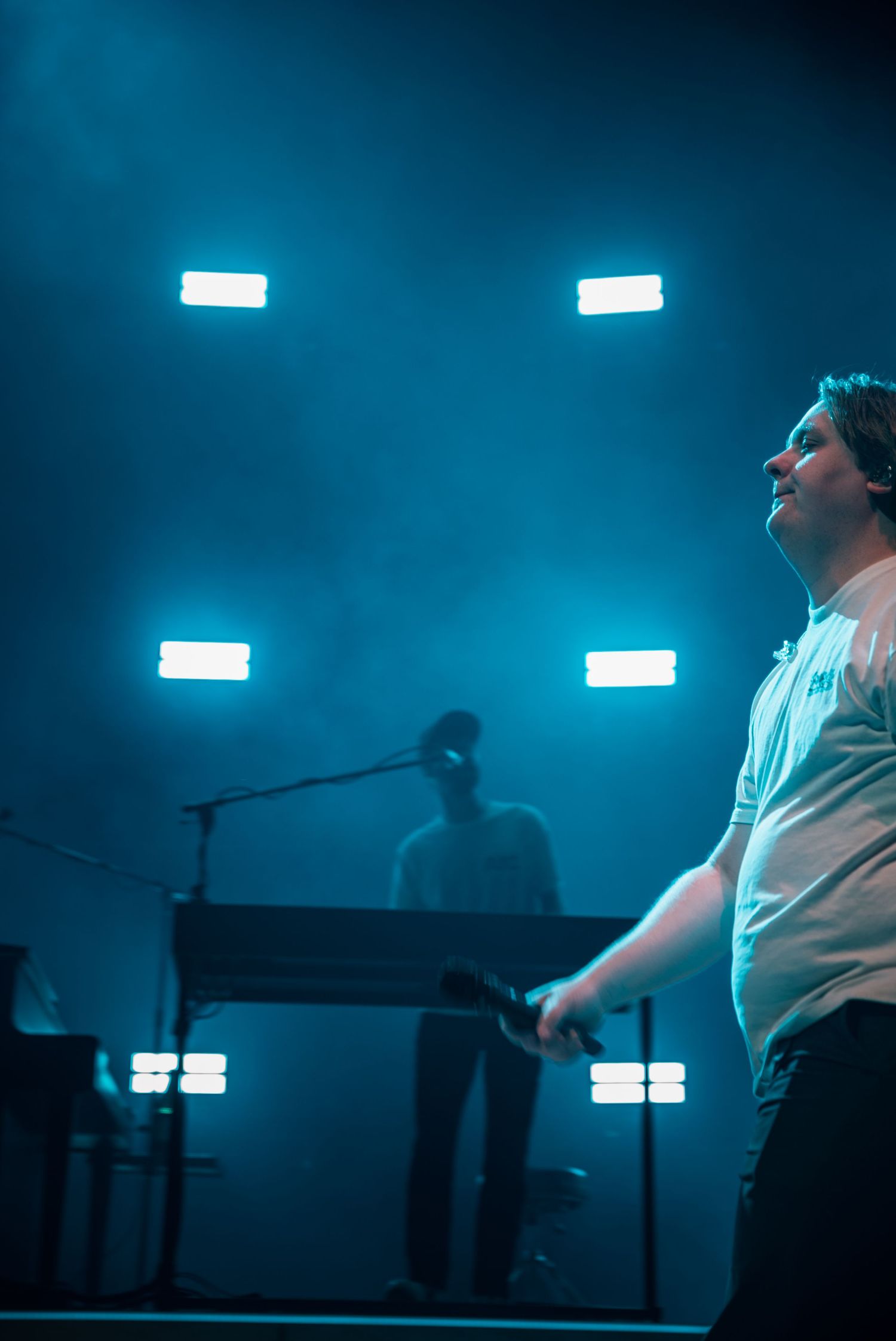 Stage performance captured in moody blue lighting with fluorescent light bars in the background.