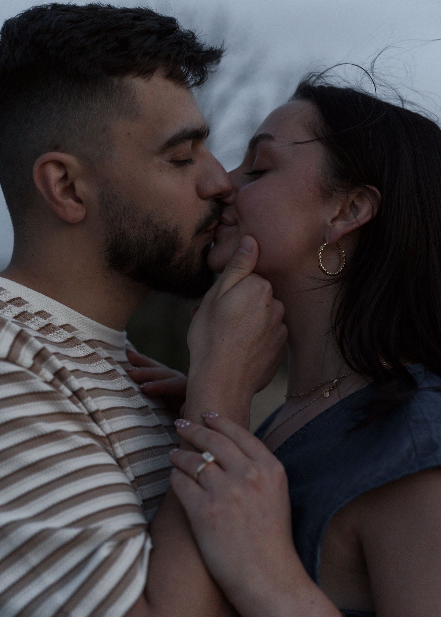 Couple sharing a romantic kiss outdoors, woman wearing gold hoop earrings and ring.