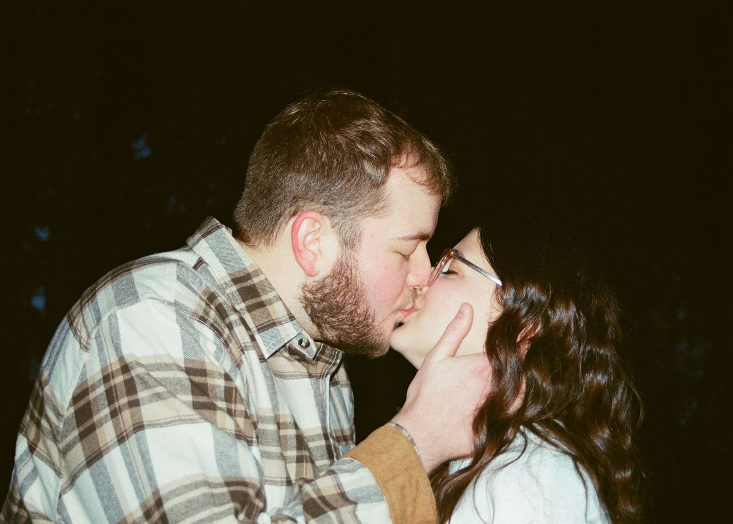 Romantic couple sharing a close kiss outdoors at night in casual clothing.