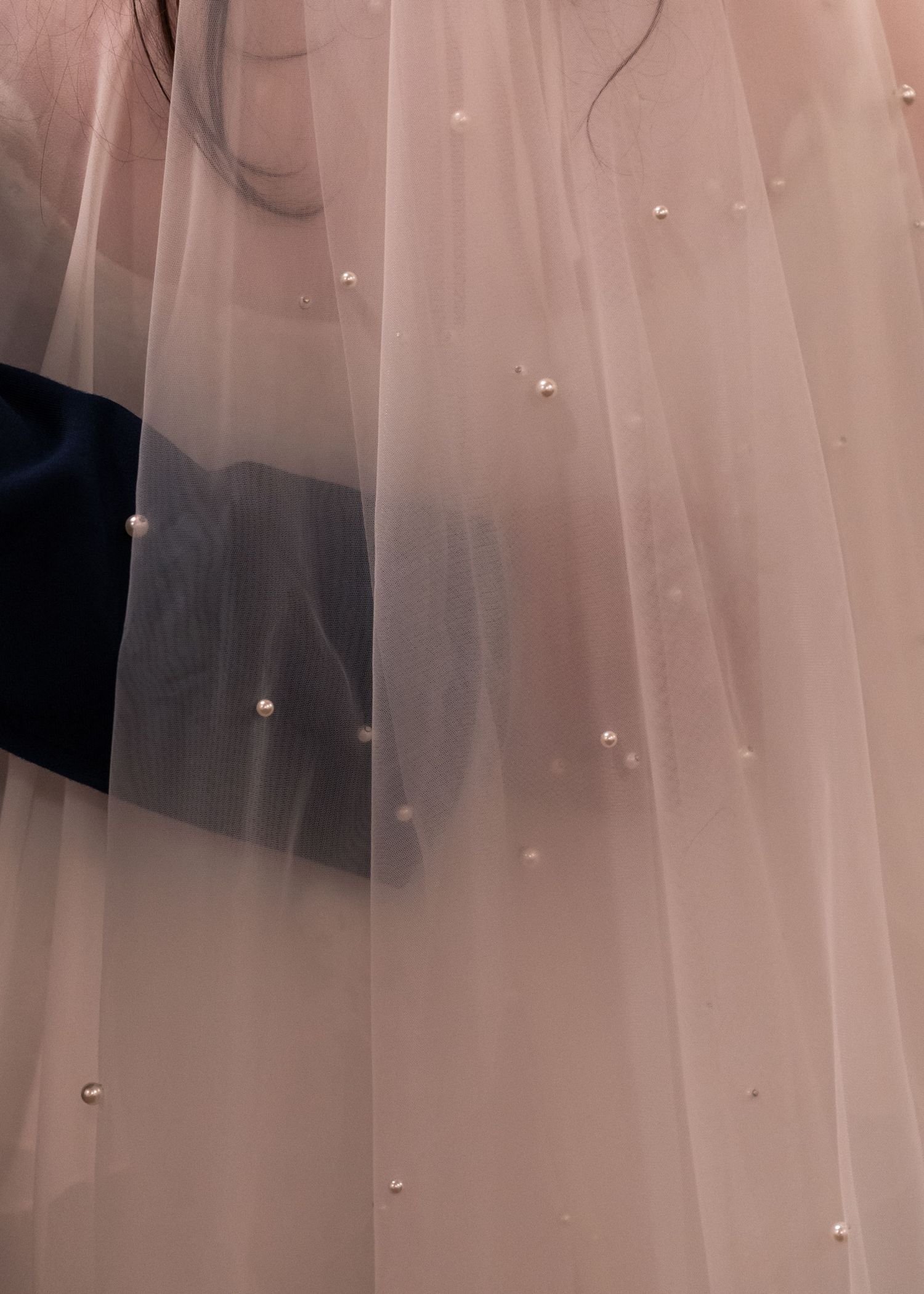 Delicate blush pink wedding veil with scattered pearl embellishments captured in soft detail.