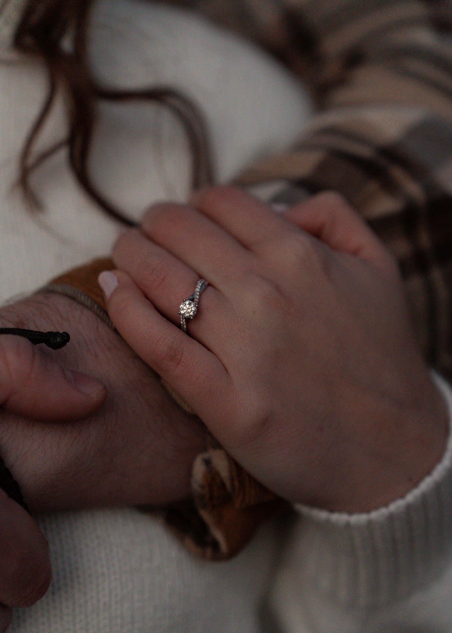 Close-up of hands showing a diamond engagement ring on woman's finger with white sweater.