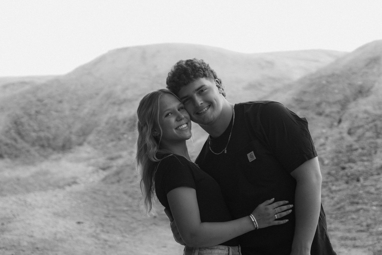 Black and white photo of a smiling couple posing together in a desert landscape setting.