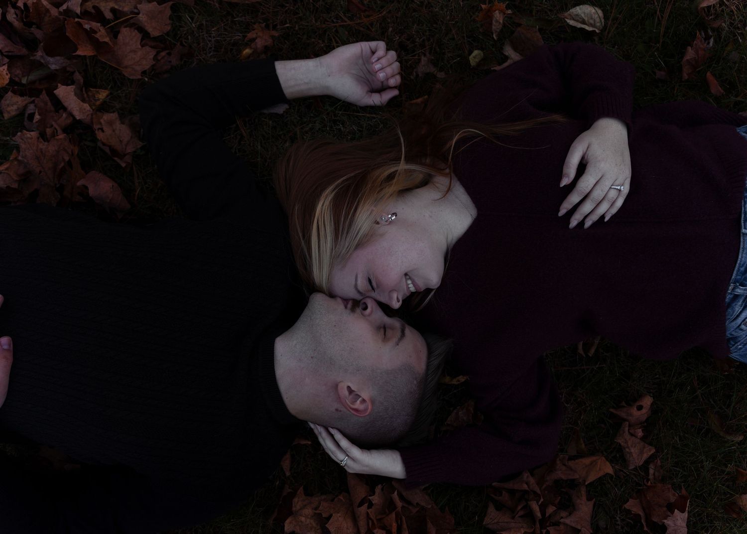 Couple lying on fallen autumn leaves gazing at each other in a romantic overhead shot.