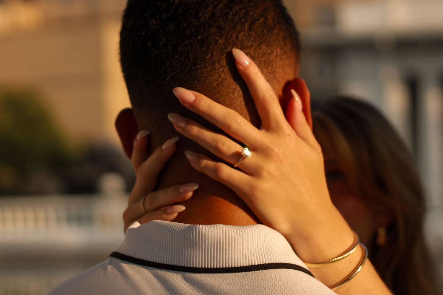 Close-up of a woman's hand with an engagement ring resting on her partner's neck.